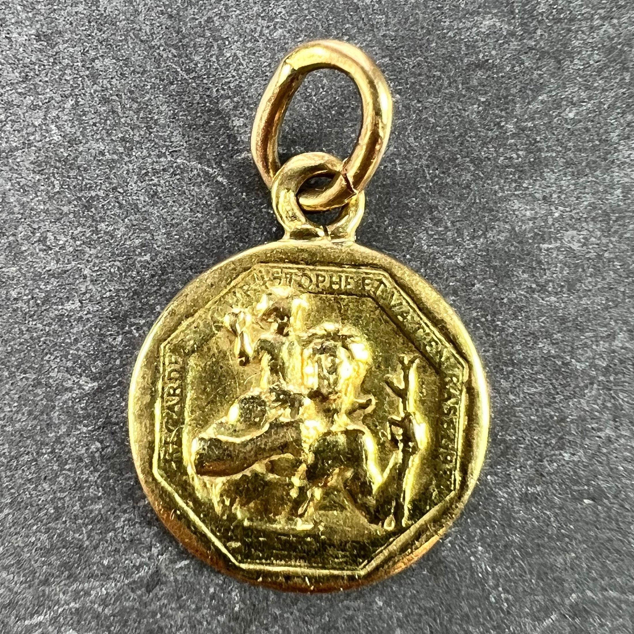 A French 18 karat (18K) yellow gold charm pendant designed as a medal depicting St Christopher as he carries the infant Christ across a river, with the motto of ‘Regarde St. Christophe et va t’en rassure' around the edge. Stamped with the eagle’s