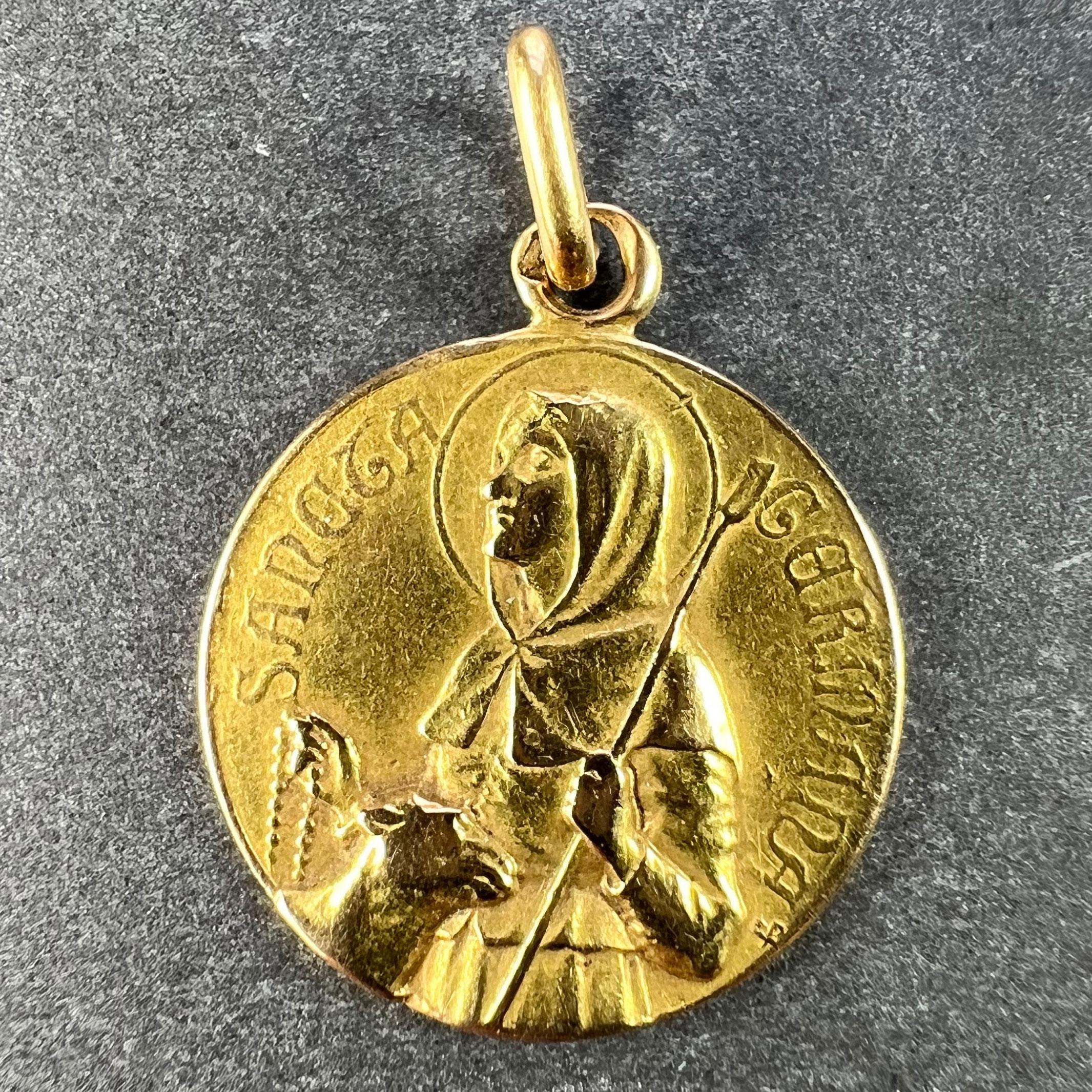 A French 18 karat (18K) yellow gold charm pendant designed as a medal depicting Saint Germaine as a shepherdess holding a rosary, with the name 'Sancta Germana' in raised letters surrounding it. The reverse depicts a lily and a spindle of wool.