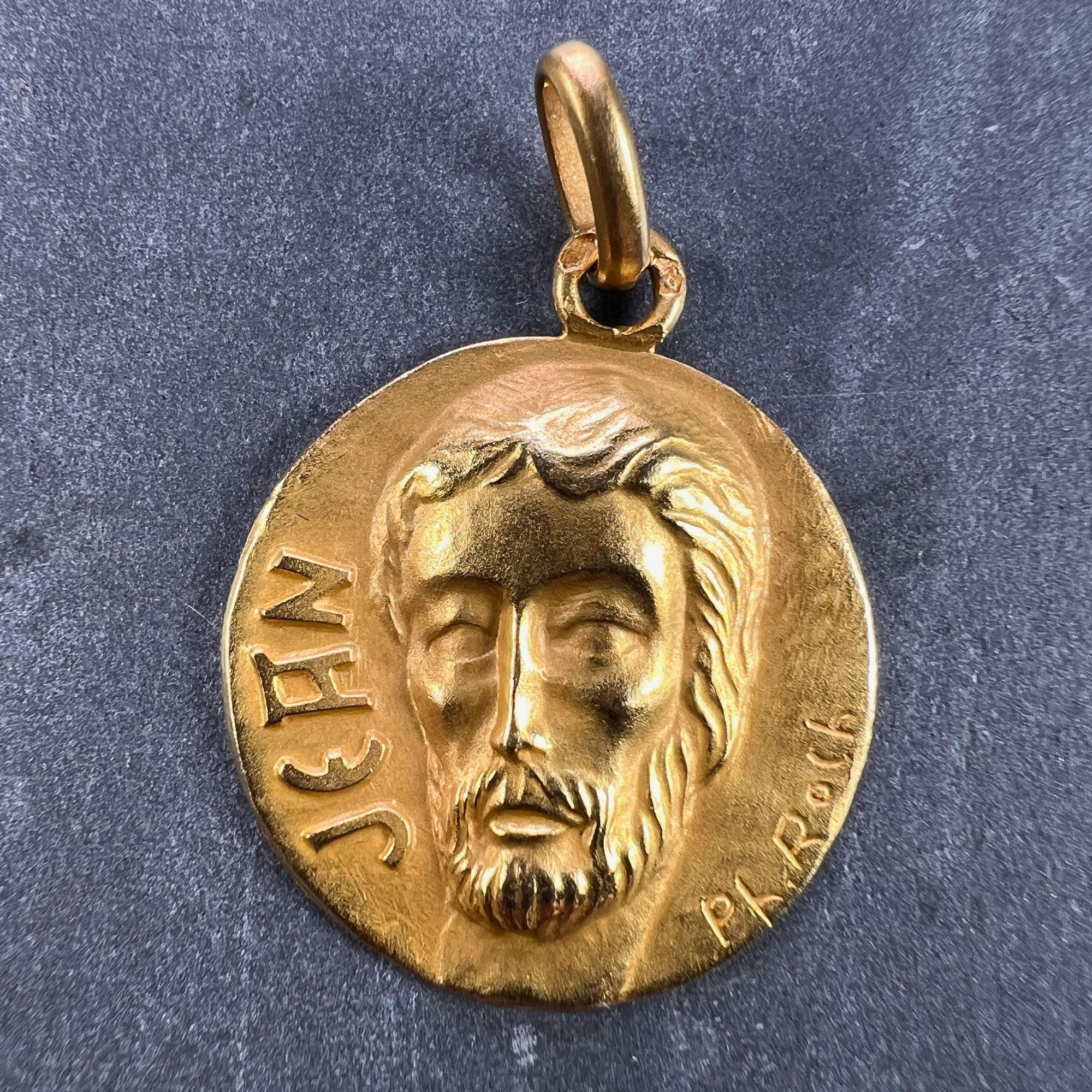 A French 18 karat (18K) yellow gold charm pendant designed as a medal representing the head of Saint John the Baptist, with the name 'Jean' in raised letters to one side. Signed PL Roch, stamped with the eagle's head for French manufacture and 18
