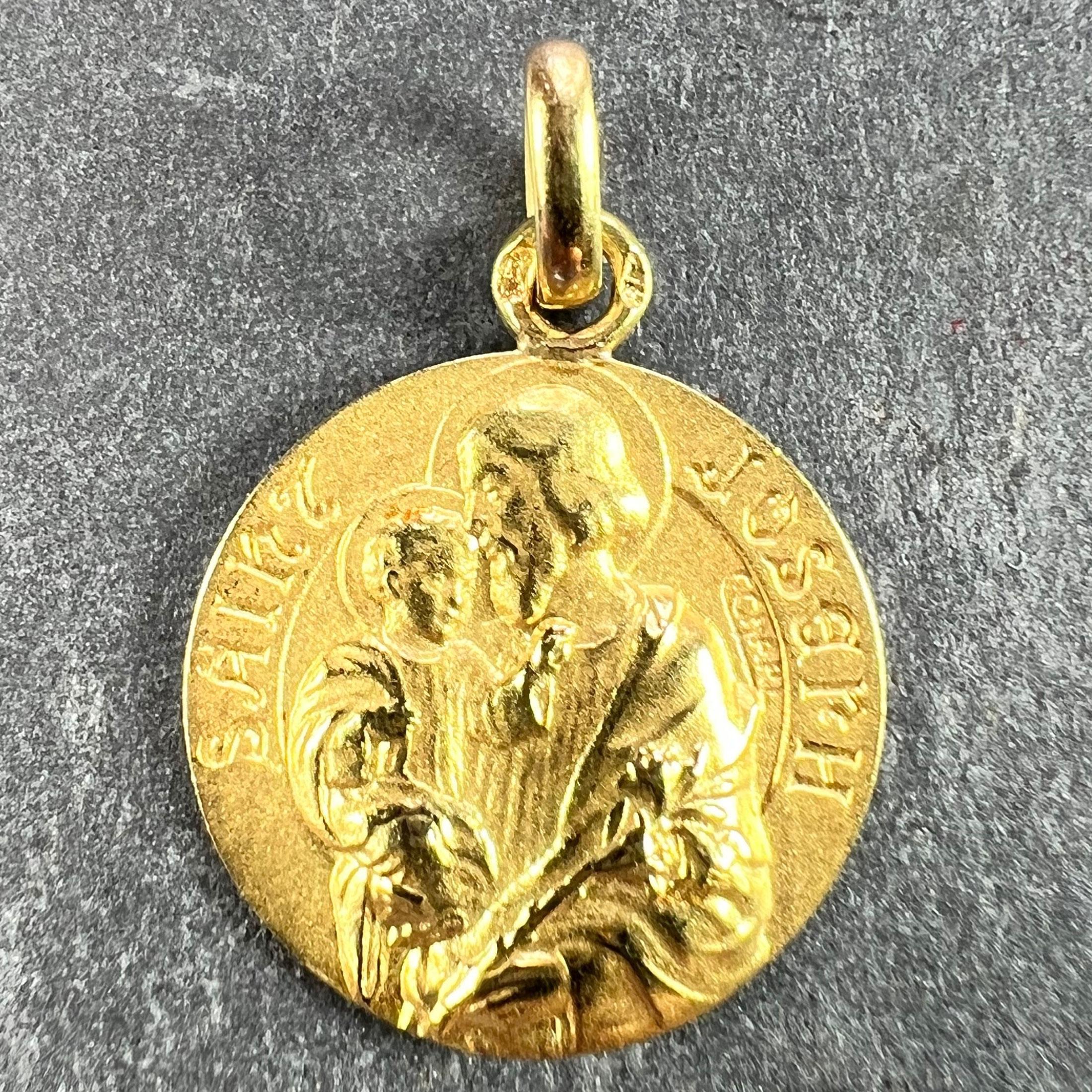 A French 18 karat (18K) yellow gold charm pendant designed as a round medal depicting St Joseph with the infant Jesus Christ, holding a sheaf of lilies. The surround reads 'Saint Joseph'. Signed C.Charl. Stamped with the eagle’s head mark for 18