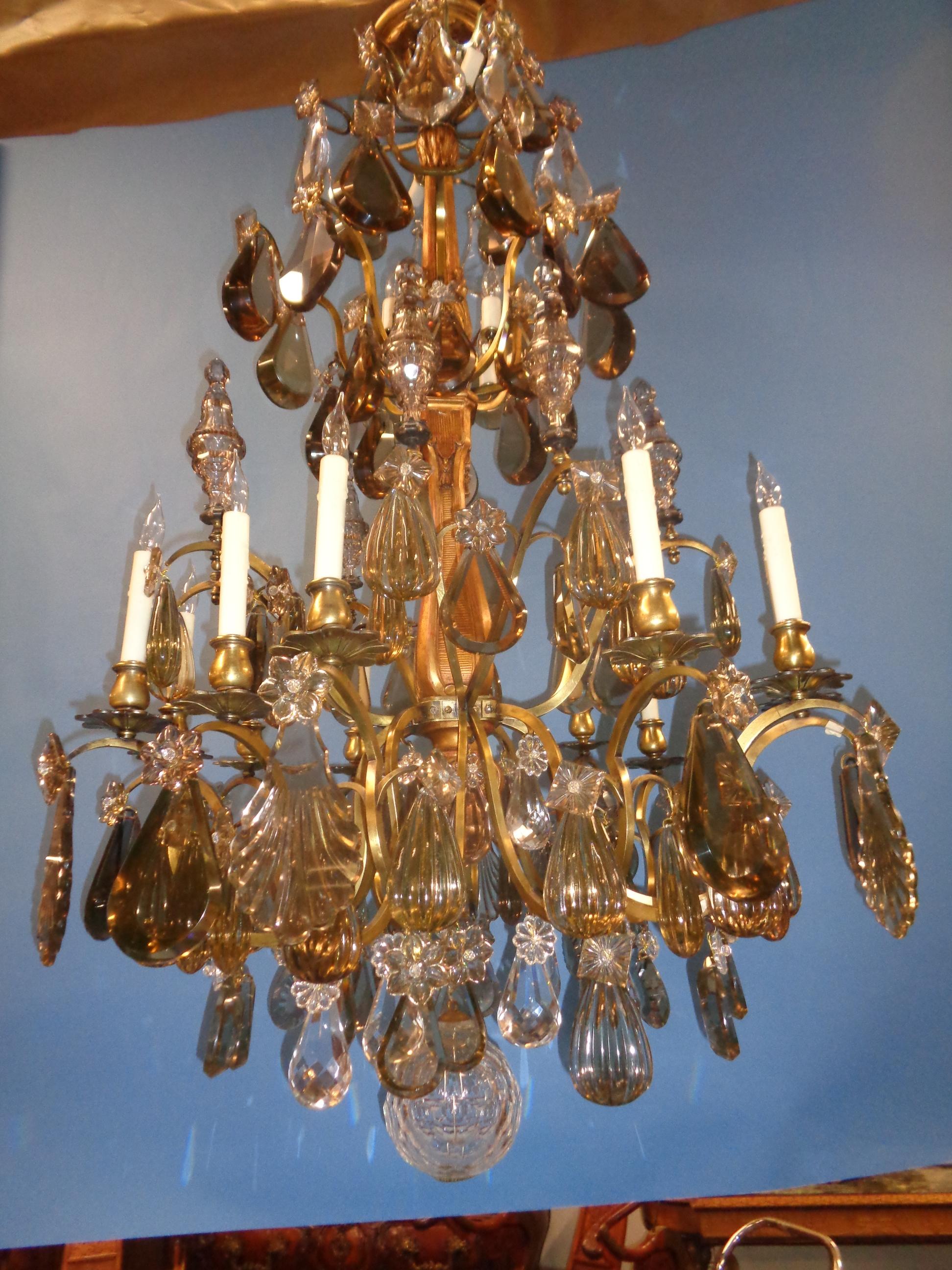 This beautiful one of a kind Saint Louis crystal chandelier has a carved and gold gilt center column with bronze and brass arms supporting multi-shaped and faceted crystals. There are six amethyst colored poignards, 12 candlelights and two tiers of