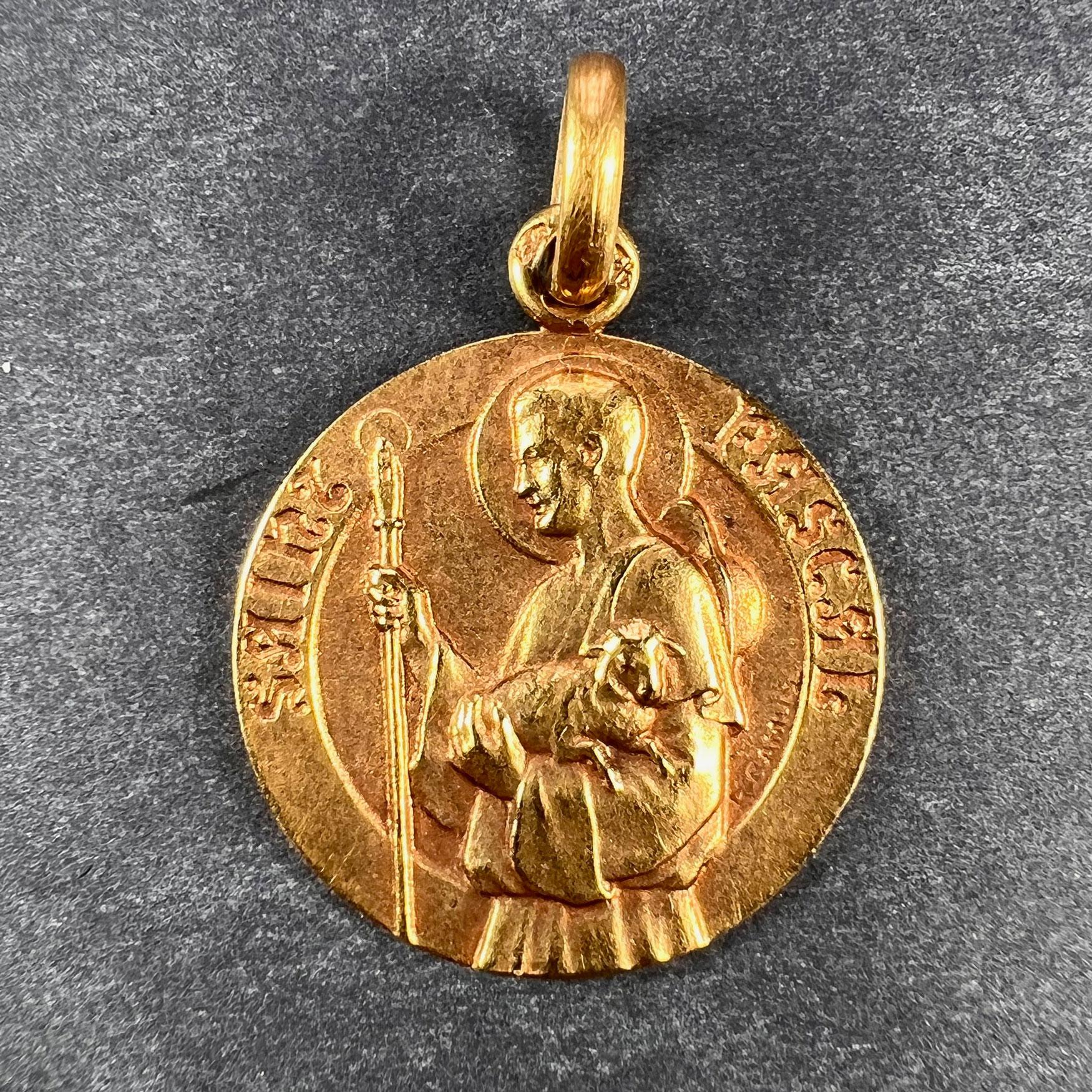 A French 18 karat (18K) yellow gold charm pendant designed as a medal depicting Saint Pascal with shepherd’s crook and lamb. Signed S. Camus, and stamped with the eagle mark for 18 karat gold and French manufacture with an unknown maker's mark. 