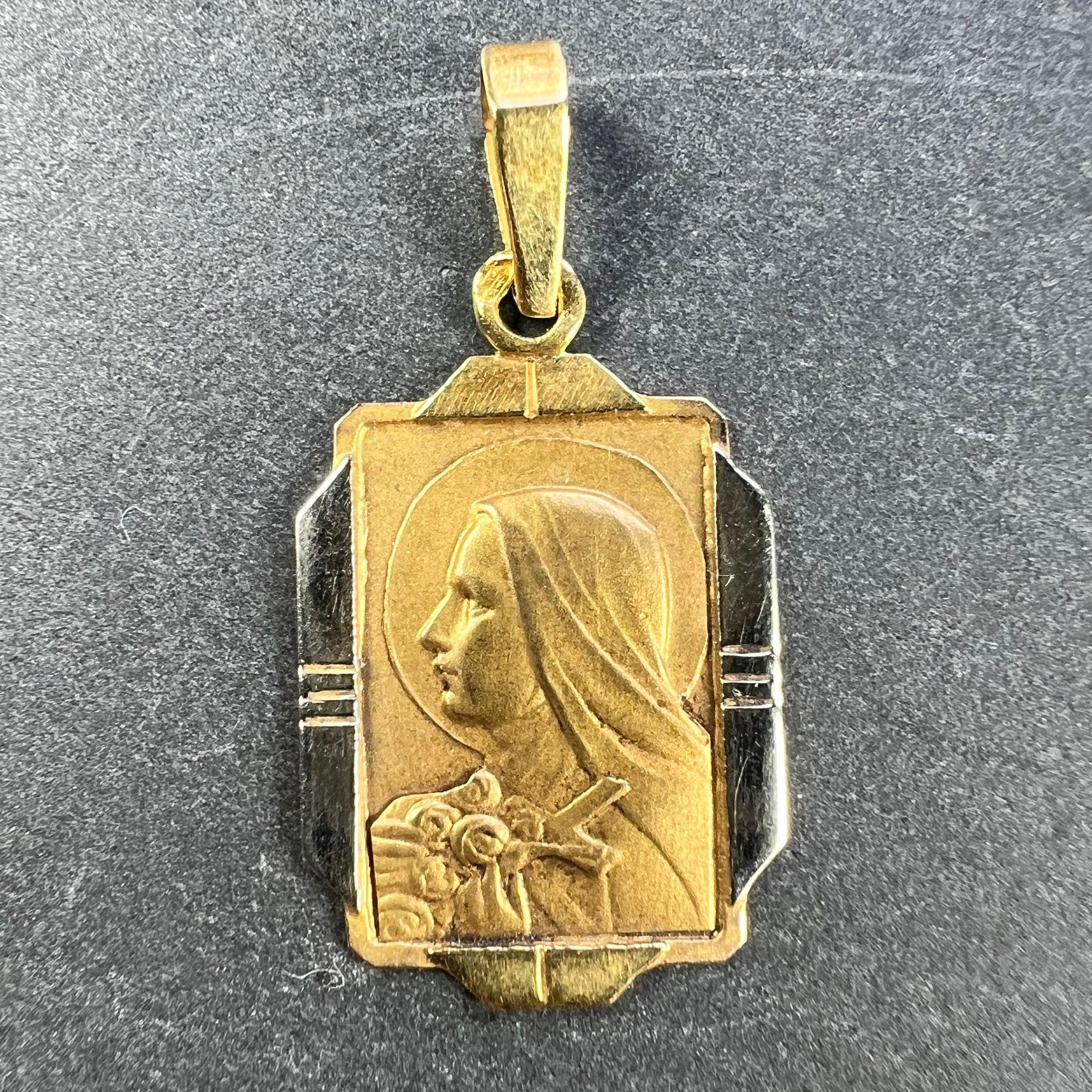 A French 18 karat (18K) yellow gold charm pendant designed as a rectangular medal depicting St Therese holding a crucifix within a sheaf of roses to a rectangular surround with a white gold ridged frame. Stamped with the eagle's head for French