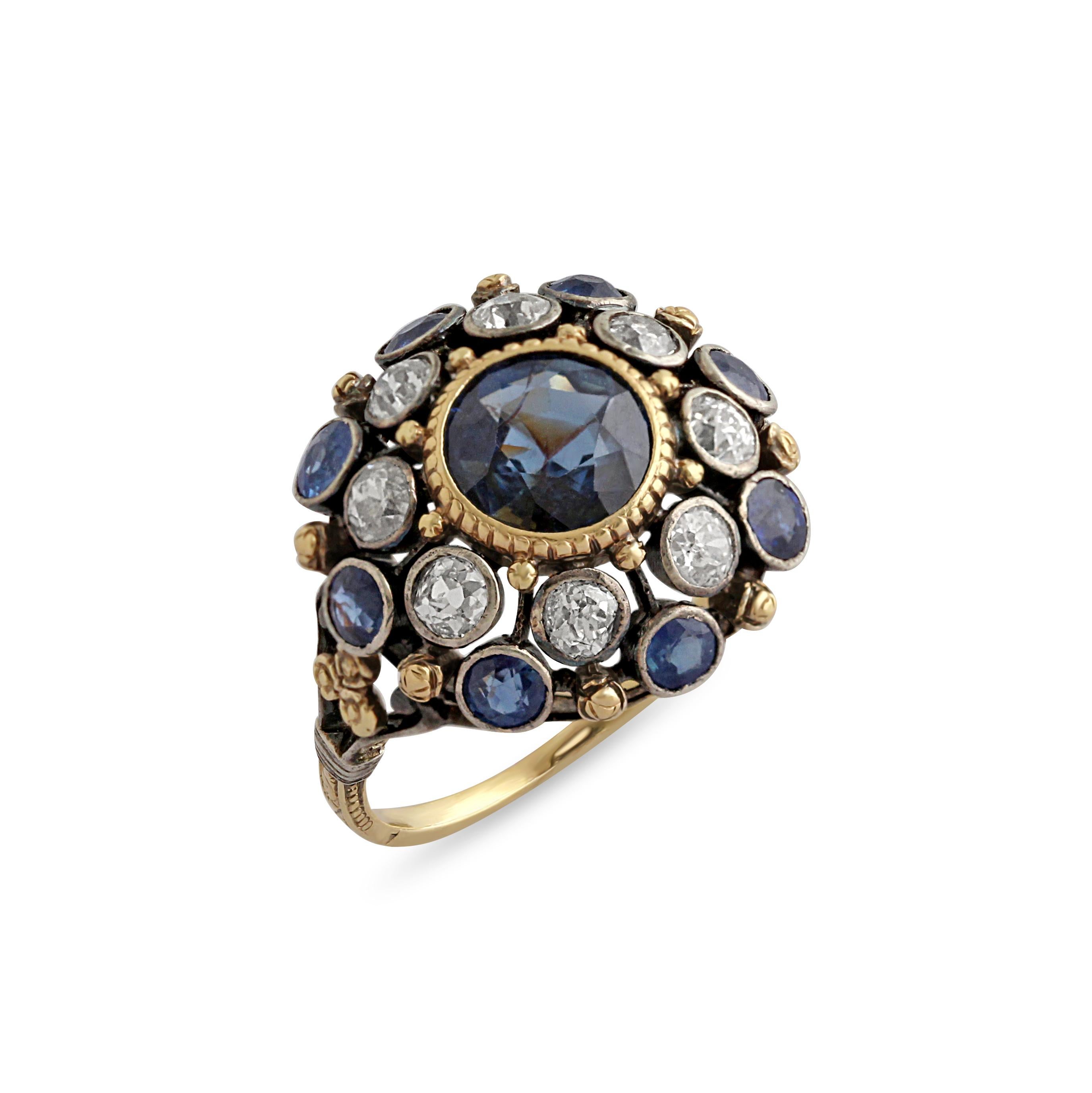 A French sapphire and diamond cluster ring, set at the centre with a round-cut sapphire with a halo of alternating bezel set diamonds and sapphires.
