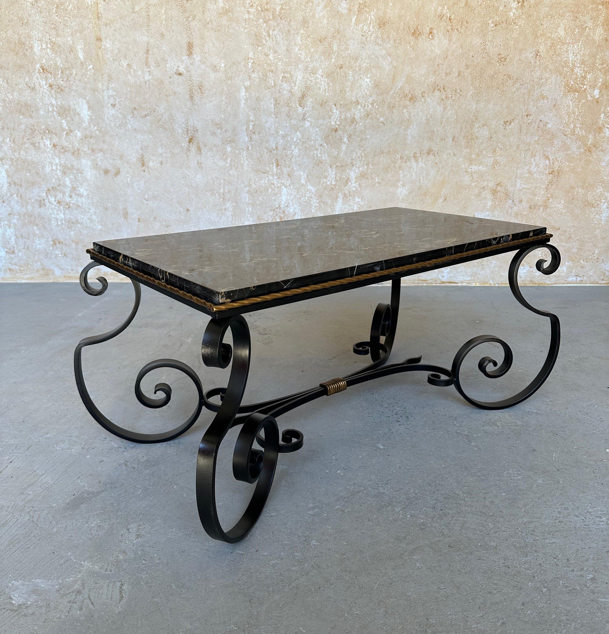 This elegant French coffee table features an ornate black frame with dramatic “S” scrolled legs and a horizontal stretcher with a collar that is highlighted in hand-applied gold. This style is typical of 1940s-50s French design. The original marble