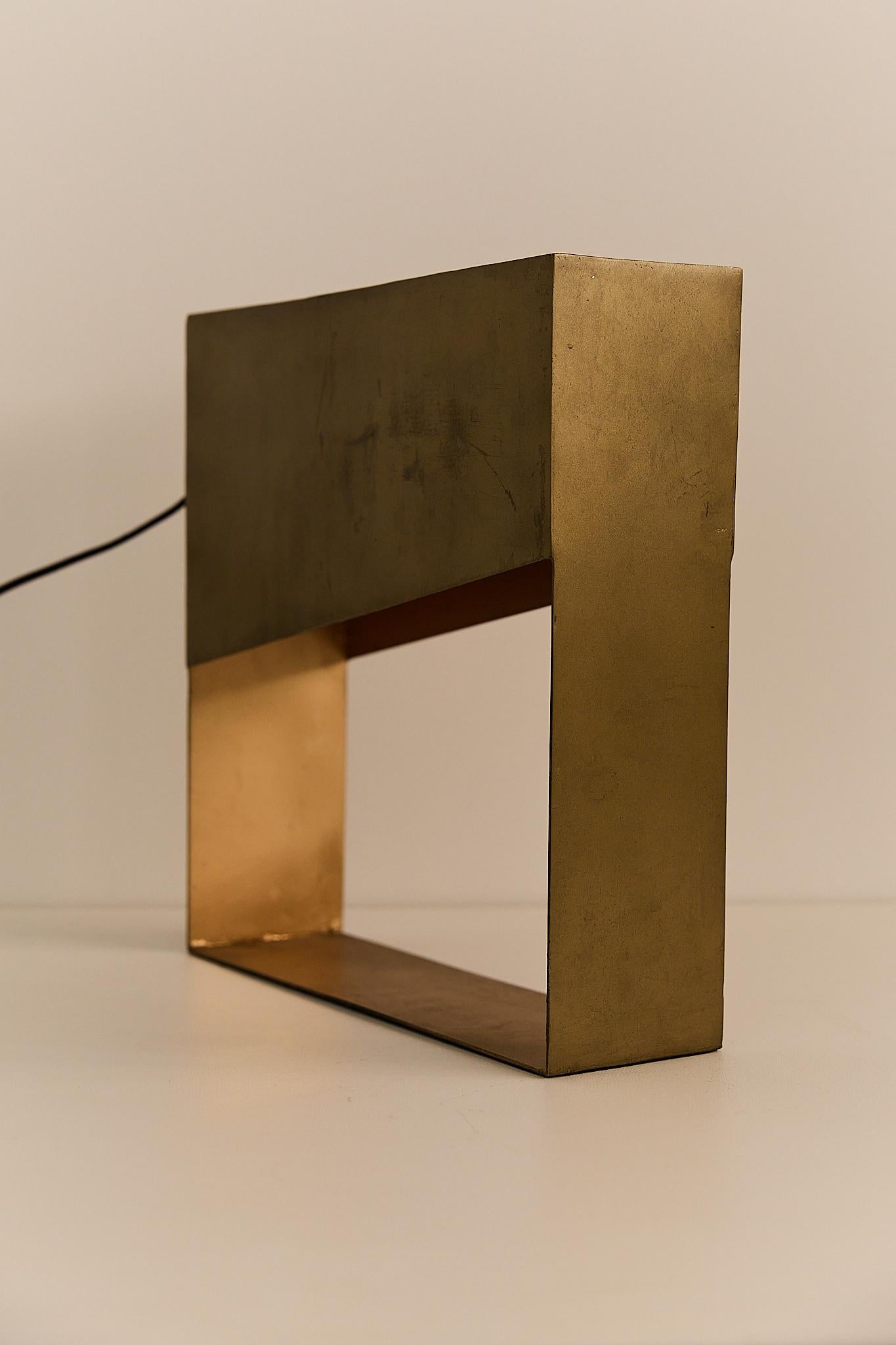 A bold geometric lamp from 1970s France, crafted in solid metal with a warm brass finish. Its sculptural, open-frame design casts a soft ambient glow