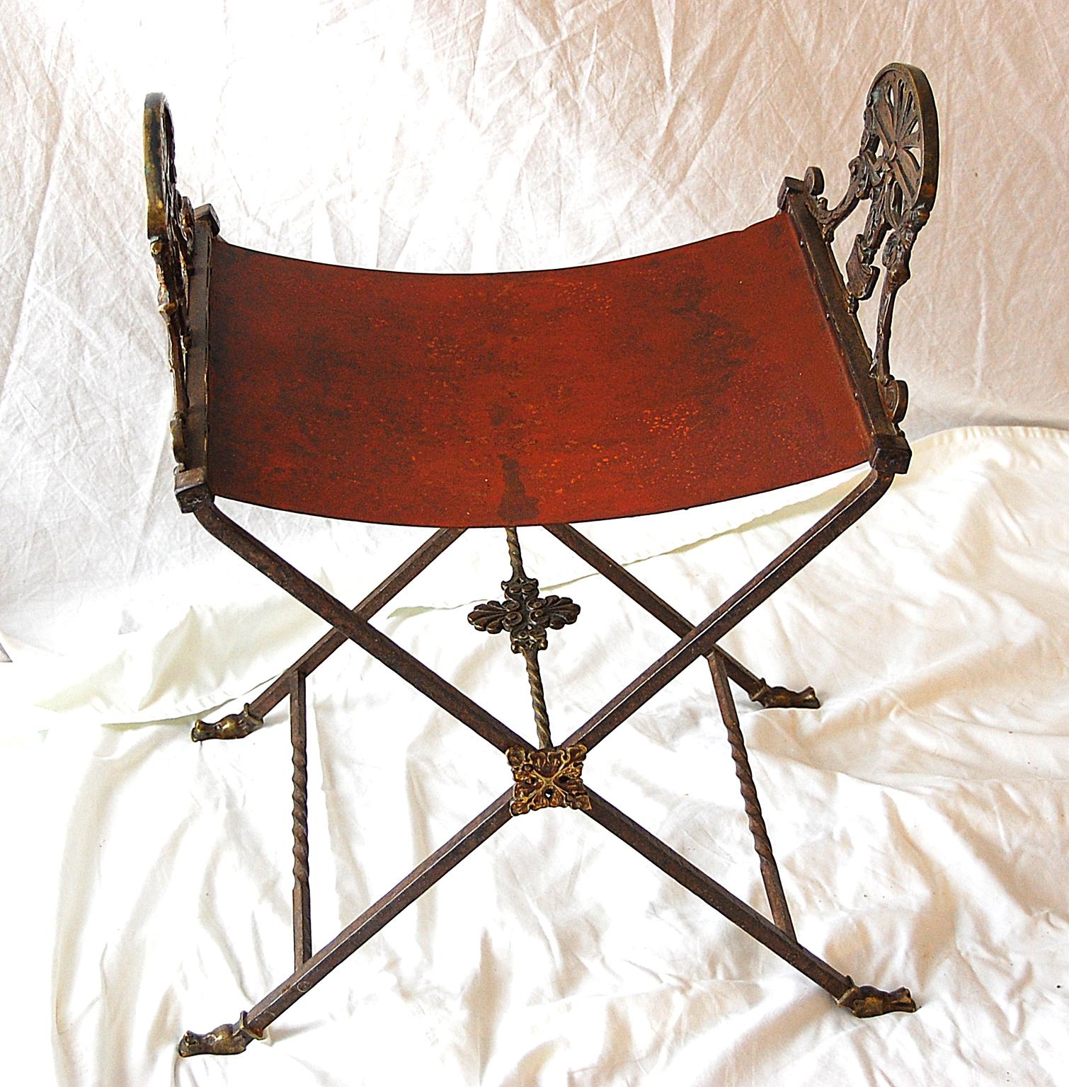 French Second Empire period cast bronze X frame stool with shaped iron seat, original finish including old red color to seat, classical heads to armrests and animal heads that terminate the X frame. This is a heavy yet comfortable stool, circa 1850.