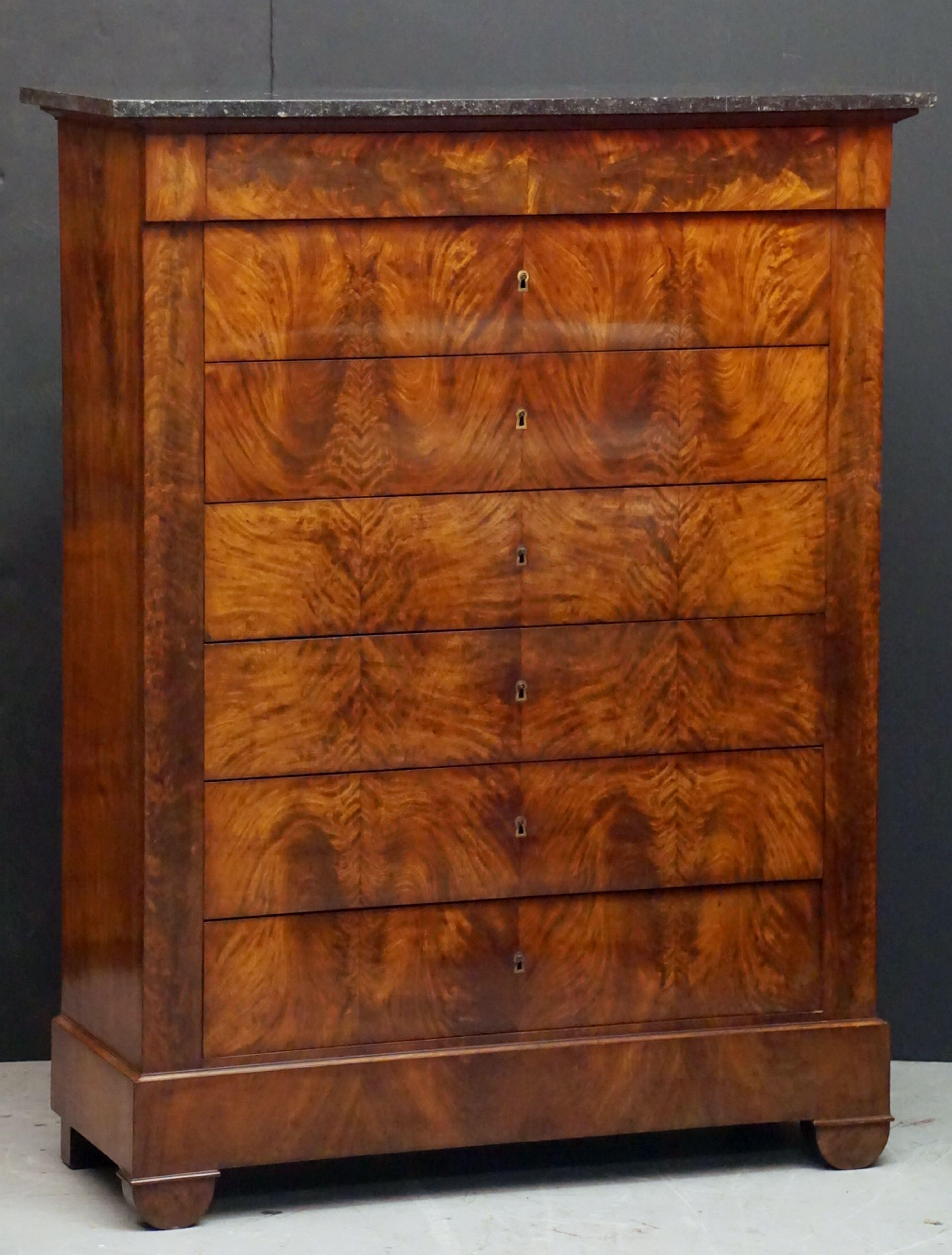 A handsome French semainier or tall chest of mahogany with marble top, featuring a slightly narrower top drawer over six larger drawers beneath.
The drawer fronts with flame-cut veneers. The six larger drawers have escutcheons and individual keys