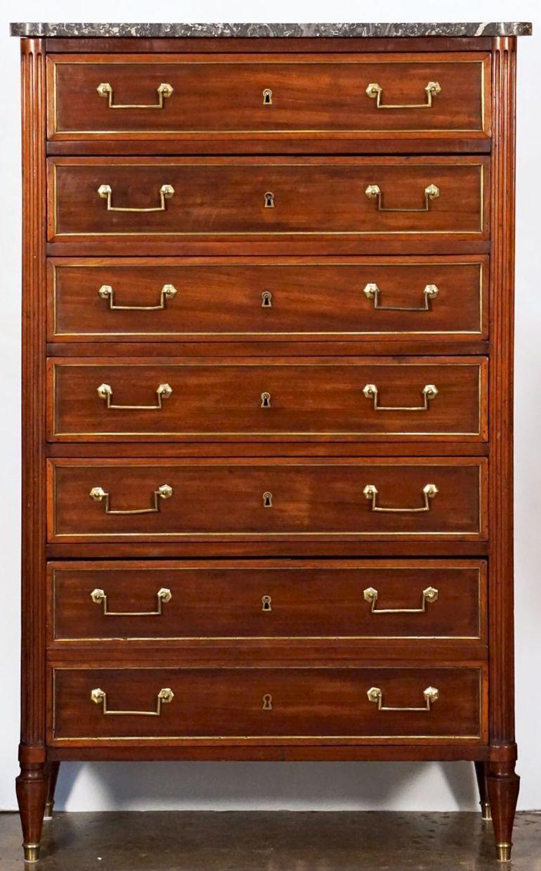 A handsome French semainier or tall chest of mahogany, c. 1820, featuring a marble top over a frieze with seven drawers between opposing columns - each drawer framed in brass and wood with brass pulls.
Set upon raised turned feet with brass