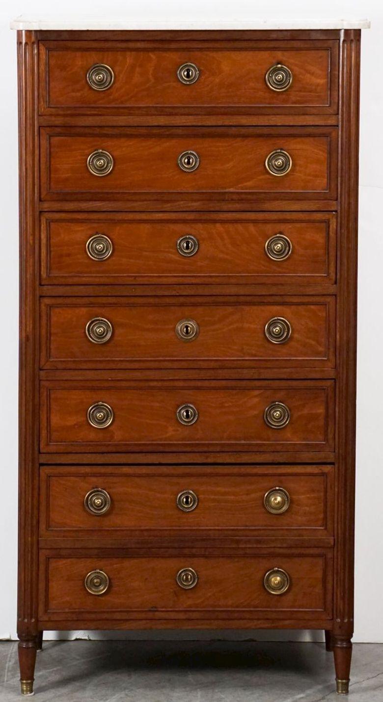A handsome French semainier or tall chest of mahogany from the late 18th century, featuring a white marble top over a frieze with seven drawers between opposing reeded columns, with paneled sides - each drawer with a beaded frame and embossed brass