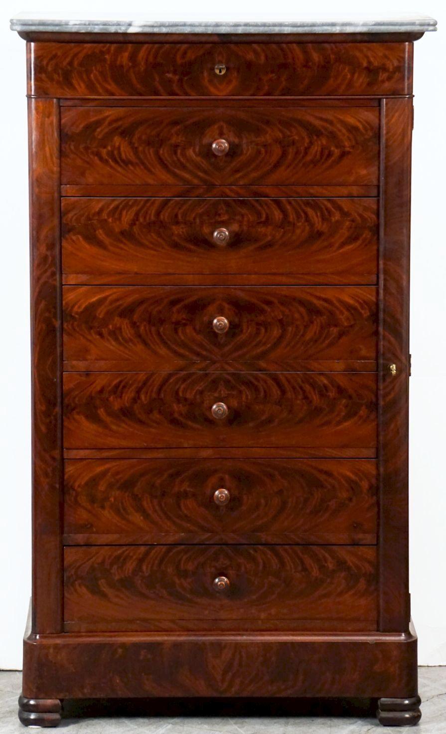 A fine French semainier or tall chest of mahogany, featuring a figured marble top over a frieze of one drawer with escutcheon over six drawers with a locking pilaster and key - each drawer showing matching flame-cut veneers and having knob pulls.