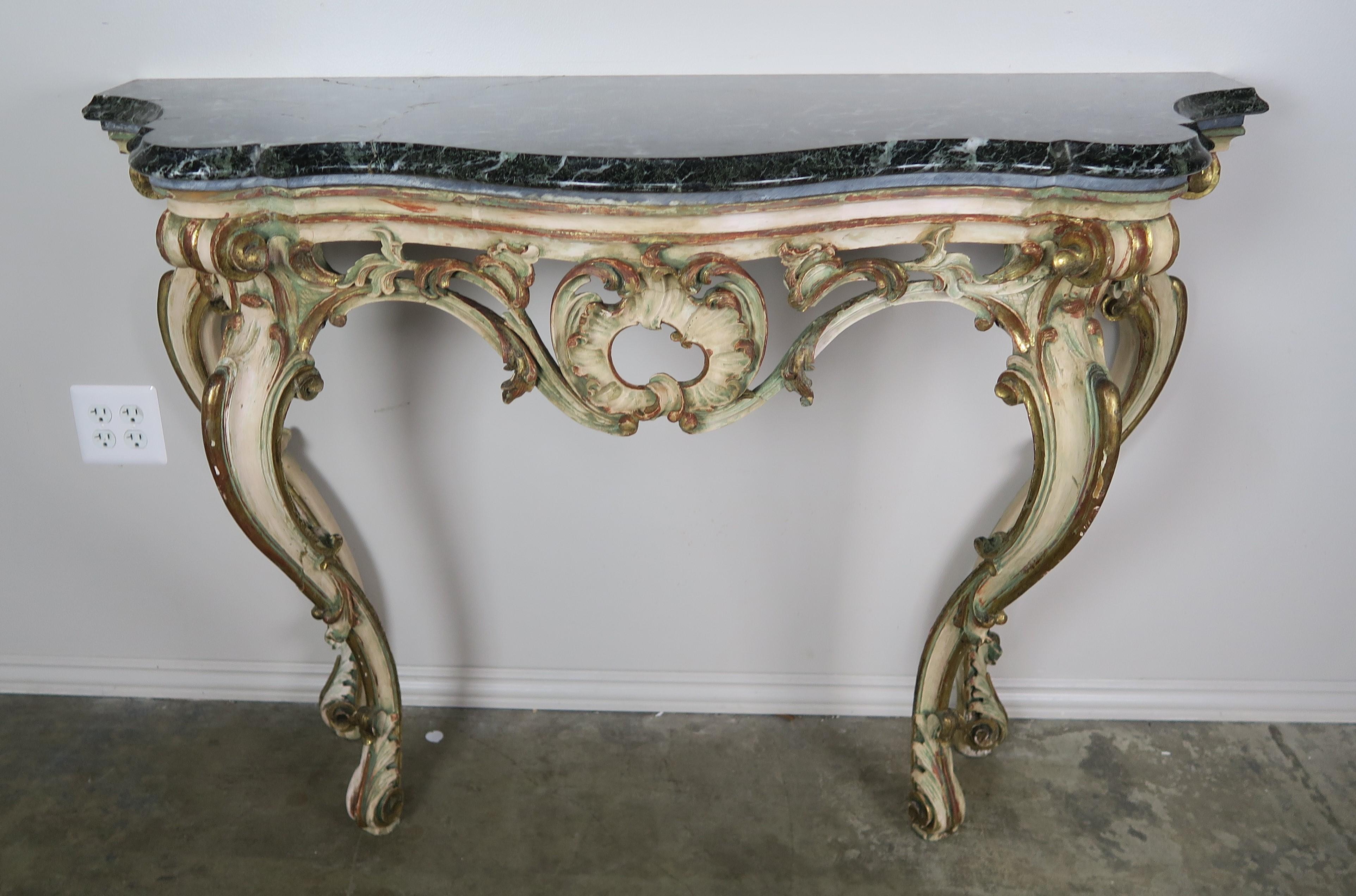 French Serpentine shaped painted and parcel-gilt console with carved center cartouche flanked by swirling acanthus leaves. The console stands on four cabriole legs that end in ram's head feet with more carved acanthus leaves. The dark green