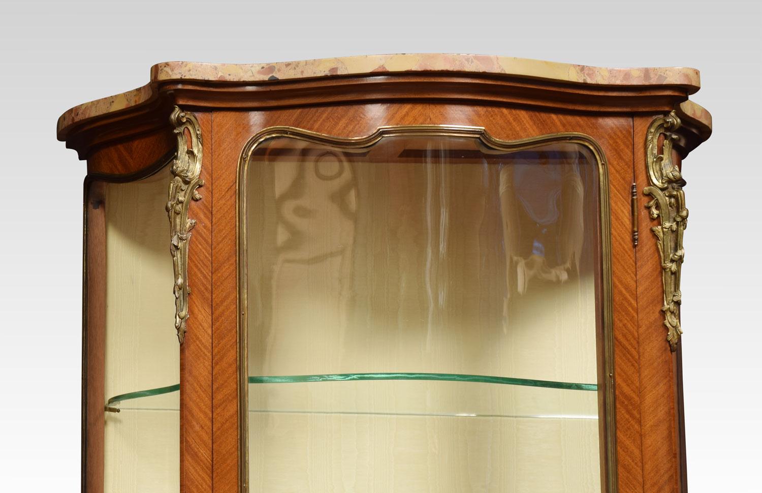 French serpentine walnut and kingwood vitrine, the shaped marble top over a three quarter glazed door with gilt metal mounted parquetry inlaid kingwood base. Opening to reveal water mark silk upholstered interior and two glazed shelves. All raised