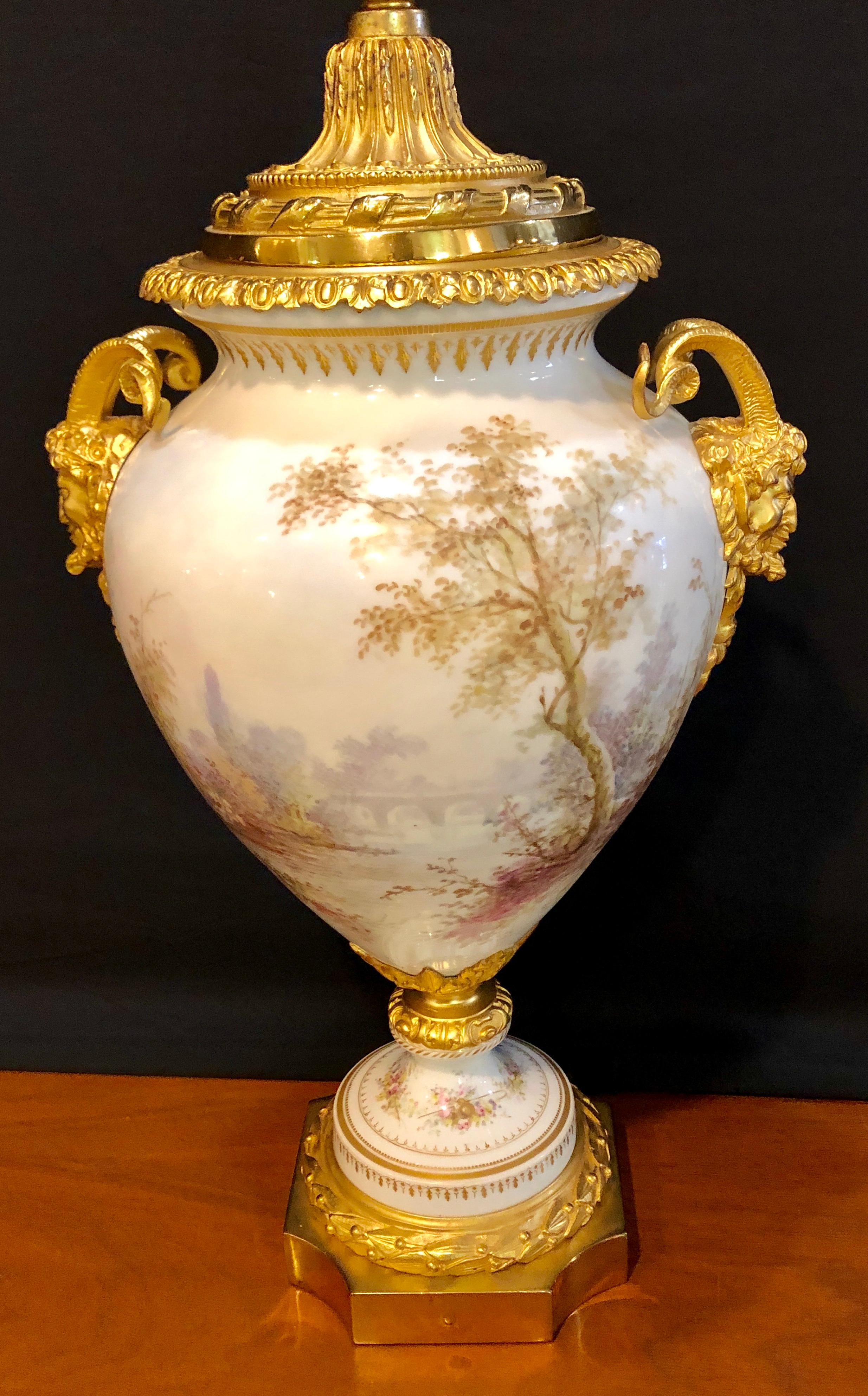 French Sevres painted ram's head bronze mounted lidded vase. This wonderfully detailed vase has been professionally cleaned on a revolving base with fine doré bronze mounts. Artist and company signed.