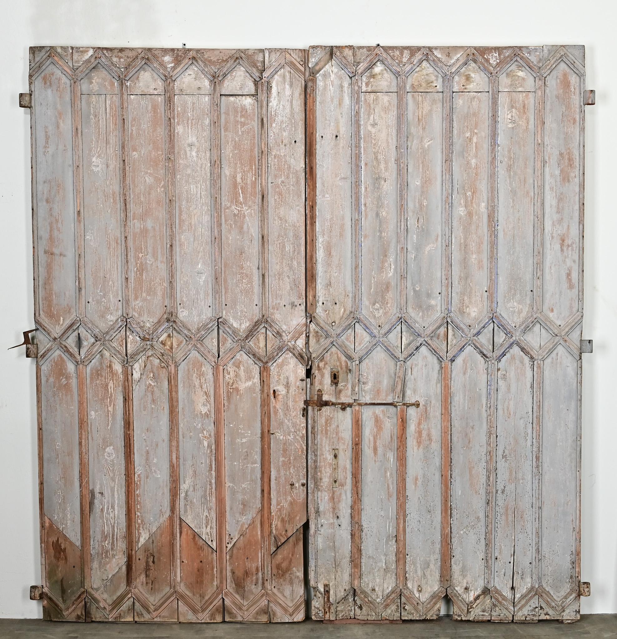Eine große Reihe von Französisch hölzernen Eingangstüren mit seiner ursprünglichen abgenutzt gemalt Oberfläche. Die Türen sind aus Massivholz mit geometrischen Holzleisten gefertigt und setzen ein Zeichen. Die Originalbeschläge aus Schmiedeeisen