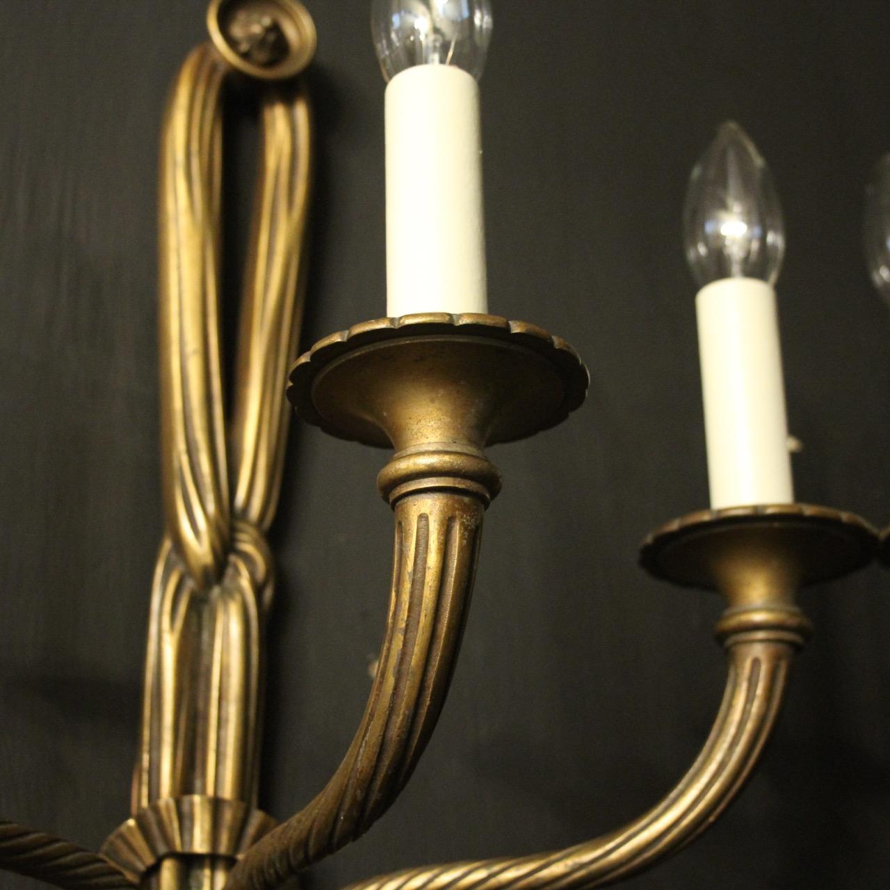 A French set of 4 dark gilded bronze triple arm antique wall lights, the reeded tapering scrolling arms with circular trumpet bobeche drip pans, issuing from a decoratively cast elongated rope and tassel pierced backplate with pierced ribbon centre