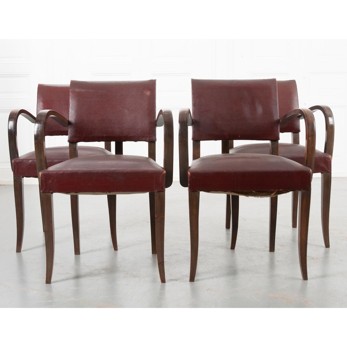 This set of comfortable upholstered arm chairs have an oak frame and great patina throughout. The dark red upholstery is slightly worn but in good condition. Round, decorative nailheads secure the fabric to the seat back and add a charming amount of