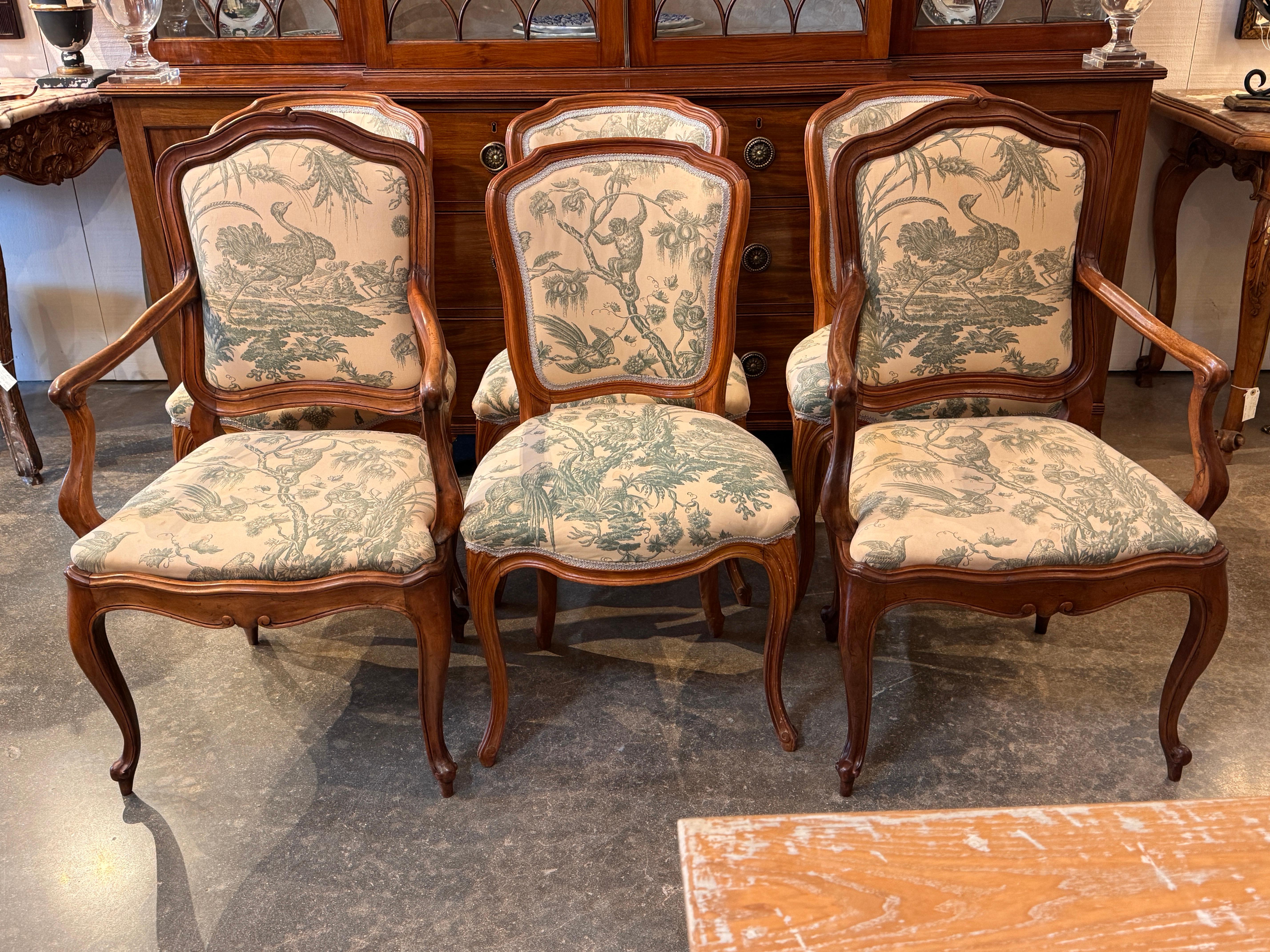 Un ensemble de six chaises de salle à manger françaises avec des cadres en noyer façonnés et des détails de tablier délicatement sculptés. Les cadres sont recouverts d'une toile pastorale. L'ensemble comprend des fauteuils latéraux et des fauteuils