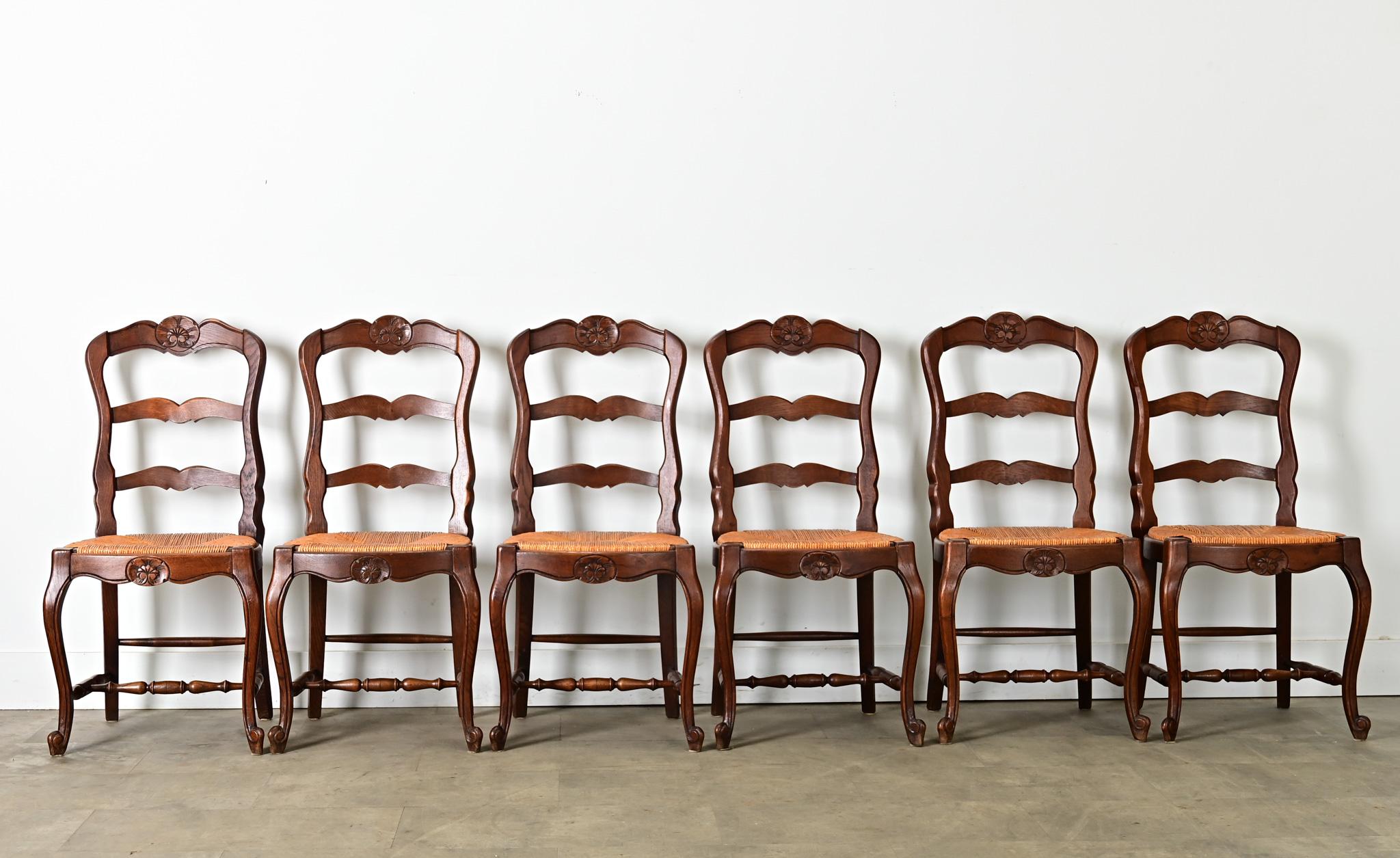 Juego de seis (6) sillas de comedor vintage de estilo Luis XV con hermosas tallas que completan los respaldos de escalera de cada asiento de junco tejido. Fabricado a mano con marcos de nogal macizo, este acogedor conjunto data de hacia 1940, pero