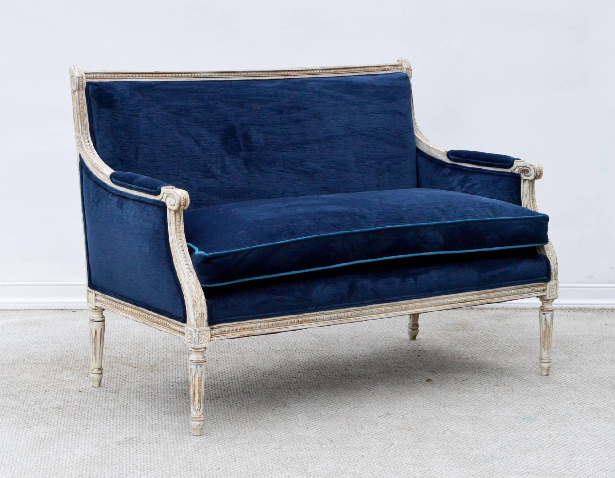 A stunning French Louis XVI style settee in navy velvet. The custom finished grey frame supports a plush and reconditioned single long down cushion. Cushion is outfitted with a subtle contrasting pipping in peacock velvet. The look is chic and
