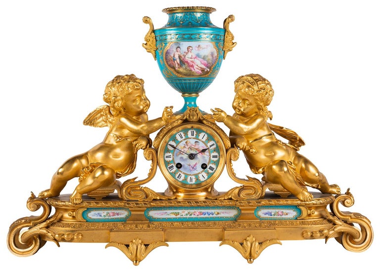 A very good quality late 19th century French Sevres style porcelain and gilded ormolu clock garniture. Having a pair of cherubs either side of the clock and central urn, classical hand painted scenes to the turquoise porcelain plaques, the clock