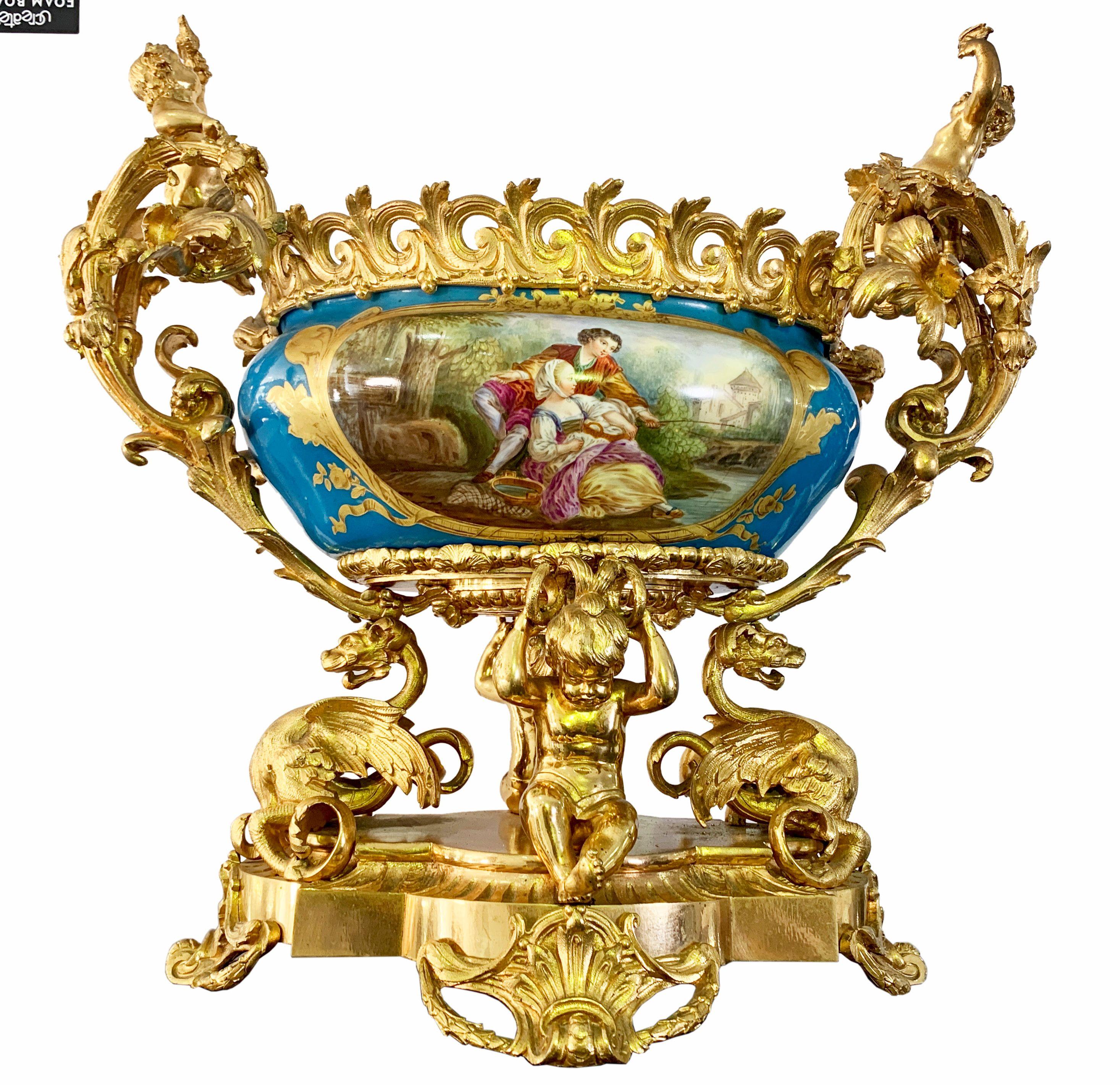 Une très belle et inhabituelle pièce centrale figurative de style Sèvres en porcelaine et bronze doré du 19ème siècle. Deux chérubins moulés tenant des oiseaux sur les poignées de la coupe en porcelaine magistralement peinte, soutenue par deux