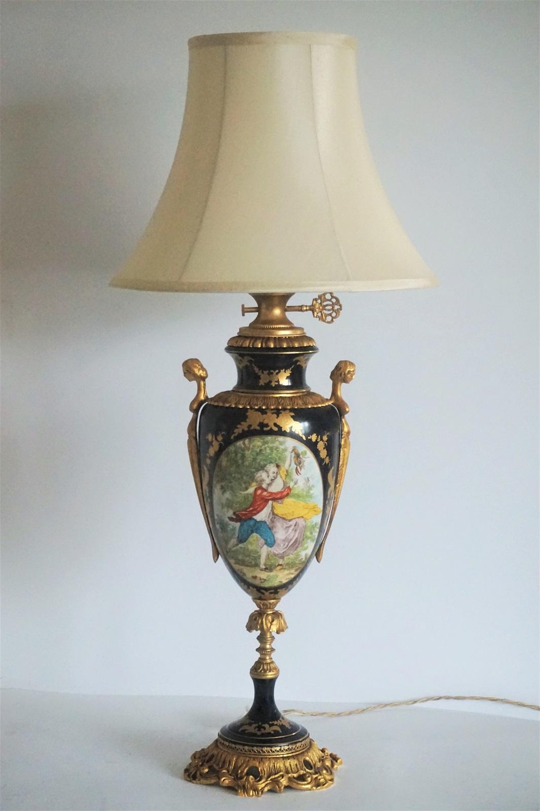A large French Sèvres style gilt bronze ormolu-mounted cobalt blue hand painted porcelain urn table lamp, first half of the 20th century. Bronze figurine handles, front side with hand painted romantic scene of young couple surrounded by gold