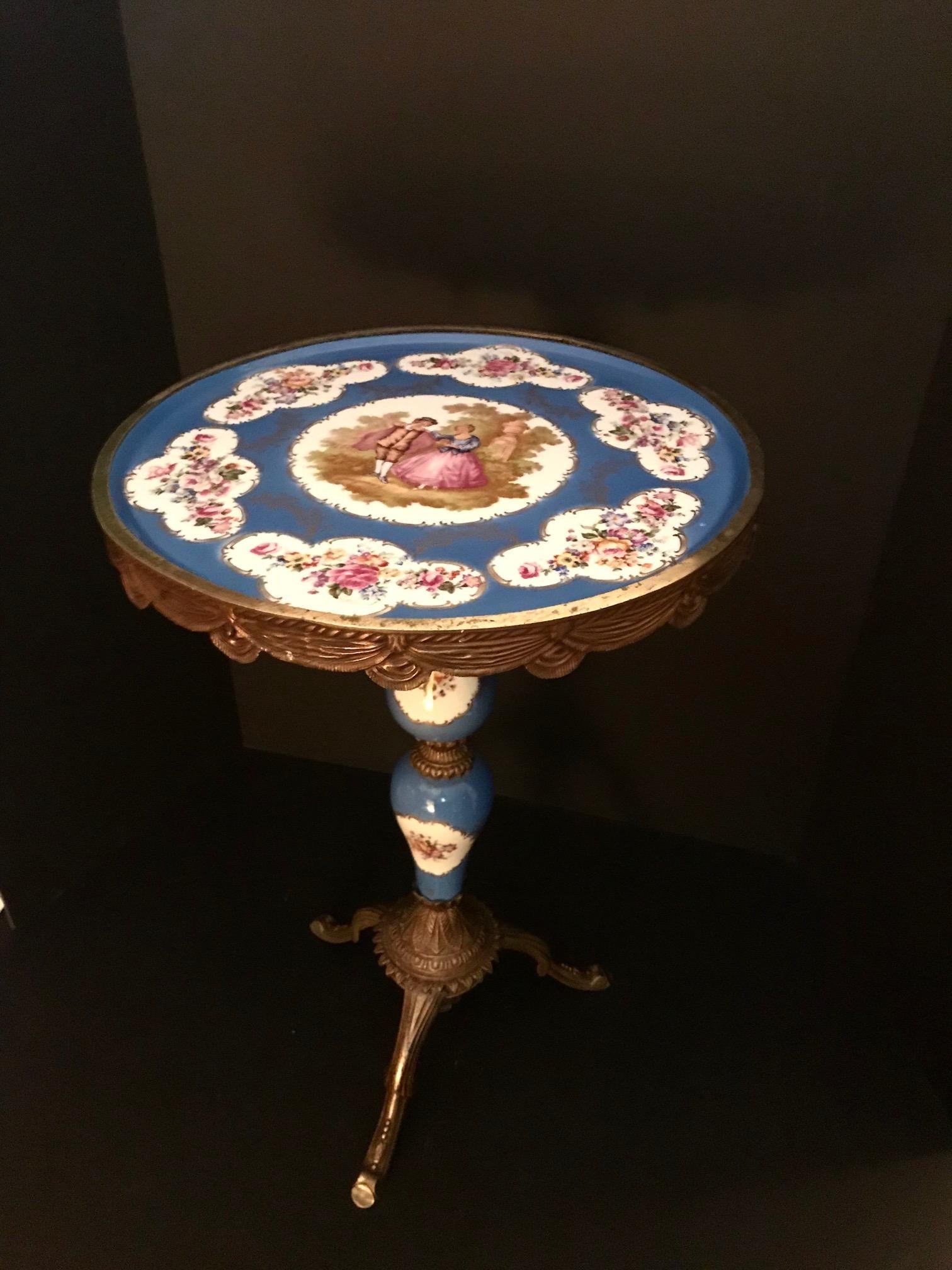 This Sevres style decorative side table has a circular top and stem decorated with transfer foliate sprays on a celestial blue ground. The centre vignette pictures a courting couple after Fragonard. This porcelain table is set in a finely gilded
