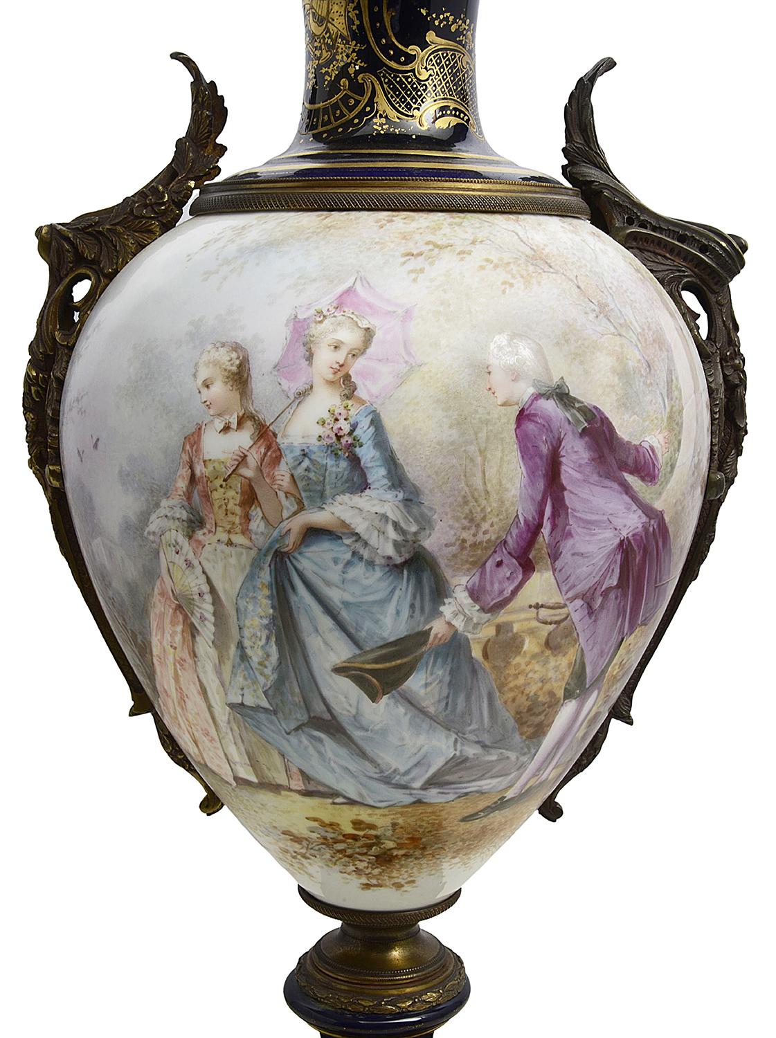 A good quality French Sevres style hand painted porcelain lidded vase, with gilded ormolu scrolling foliate mounts, cobalt blue ground with scrolling gilded decoration, the central scene depicting a courting couple with a chaperon.