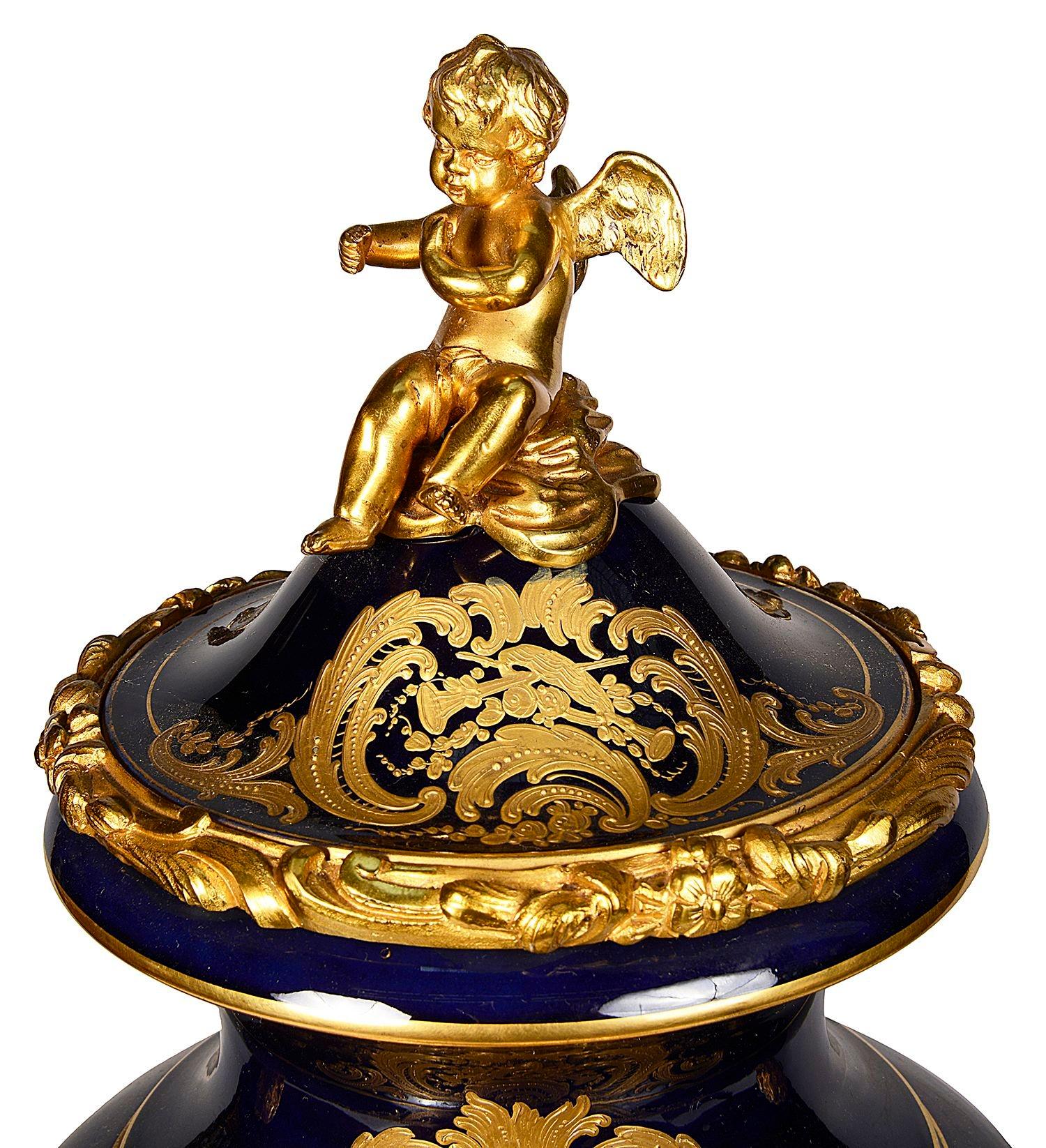 A very good quality late 19th Century French Sevres style porcelain lidded vase / clock. Having wonderful gilded ormolu mounts, a cherub finial and monopodia handles, an enamel faced eight day duration, hourly striking clock. Hand painted romantic