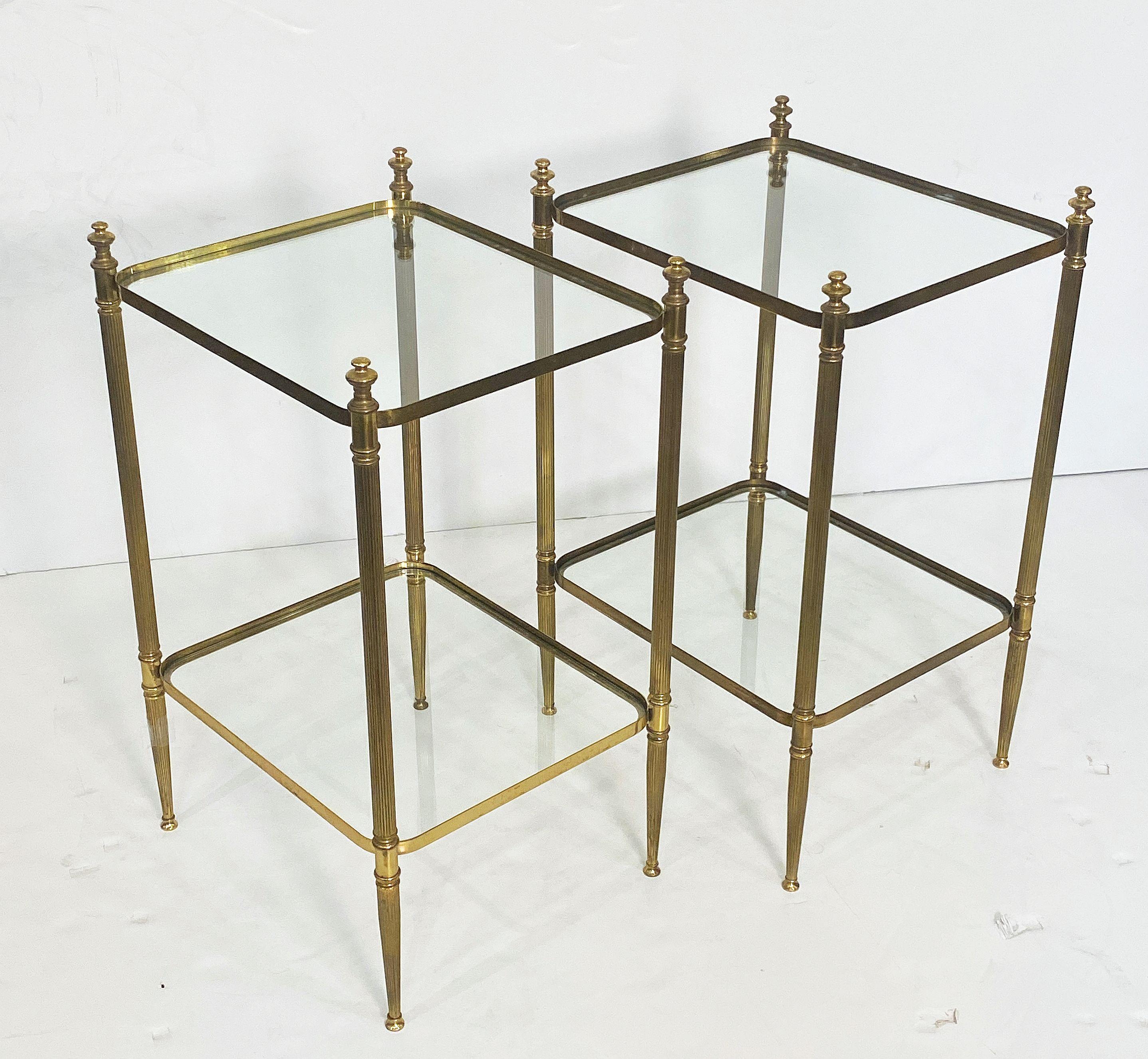 A pair of fine French Mid-Century two-tiered side or end tables - each table featuring two rectangular glass panels with rounded corners inset upon a brass frame with finial accents and reeded, tapering legs

Dimensions: Height 26 1/4 inches x