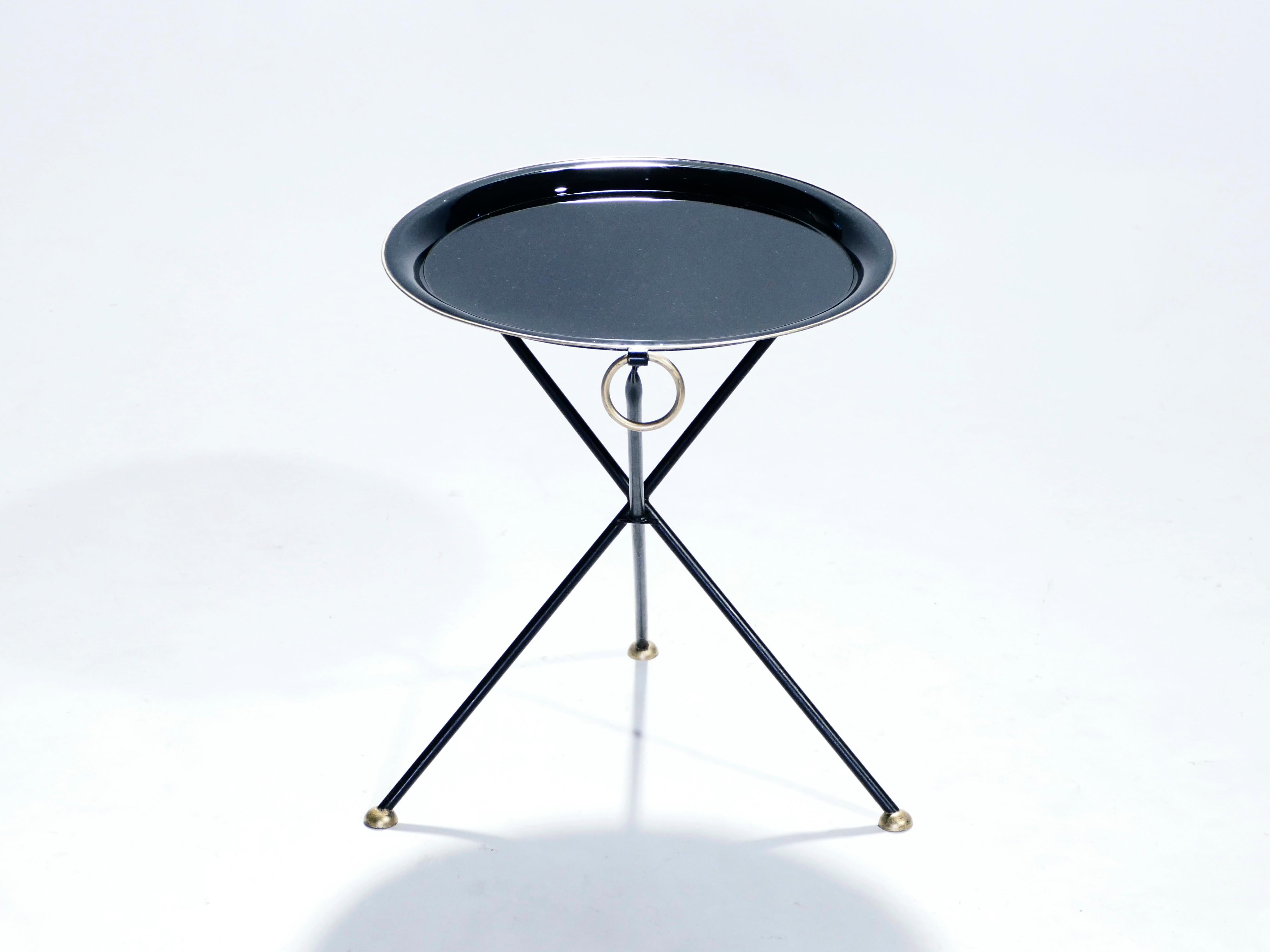 Signed by designer Christian Dior, this compact folding side table has the sleek appeal of Mid-Century Modern design and a timeless look influenced by neoclassical style. The three black metal feet are thin and minimalistic, crossing over each