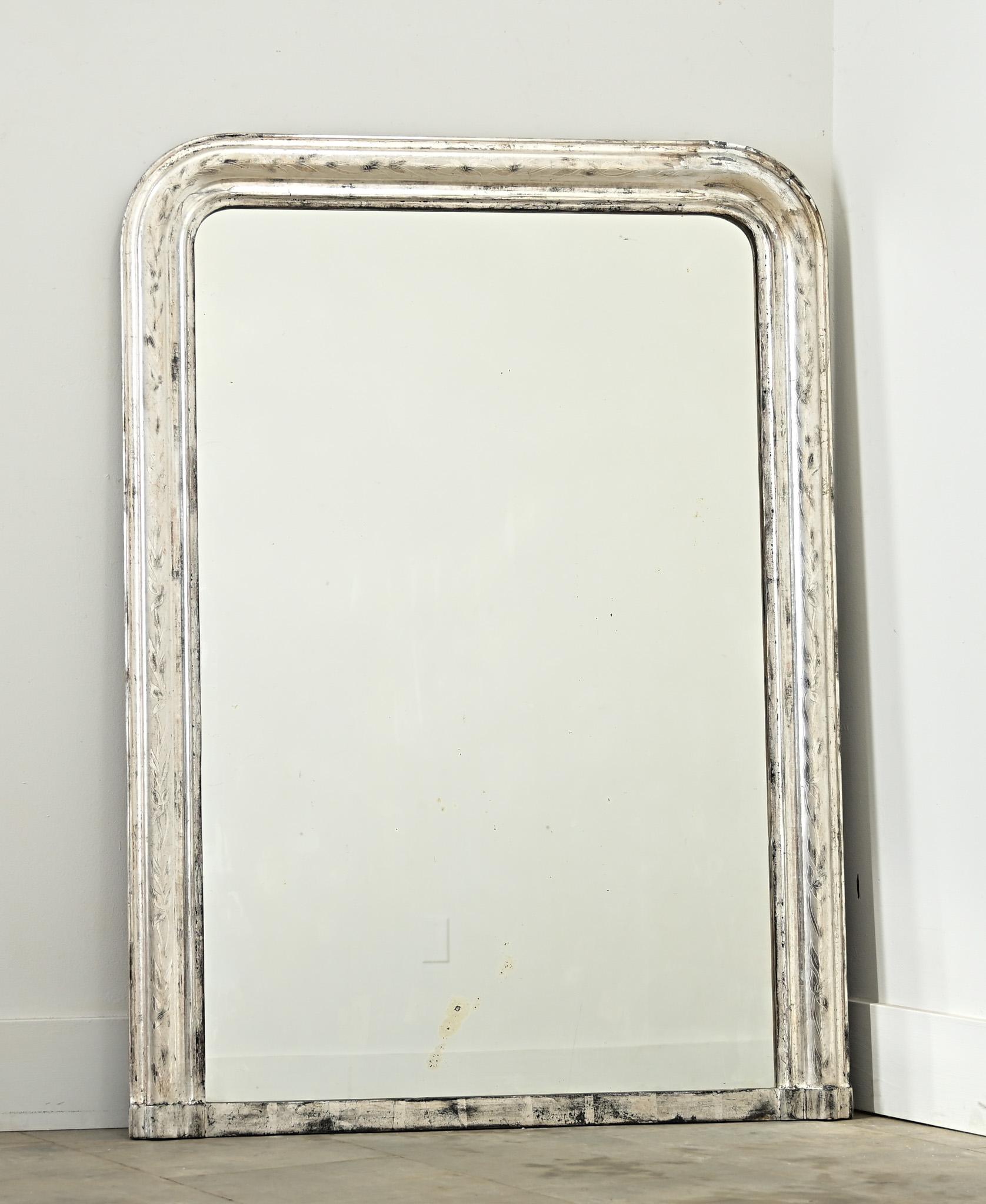 Specchio da camino Louis Philippe del XIX secolo, con una cornice in argento dorato, sobria e impreziosita da un'ossidazione scura e da una trama craquelure. Sulla cornice è inciso un elegante motivo floreale a scorrimento, simile a un iris,