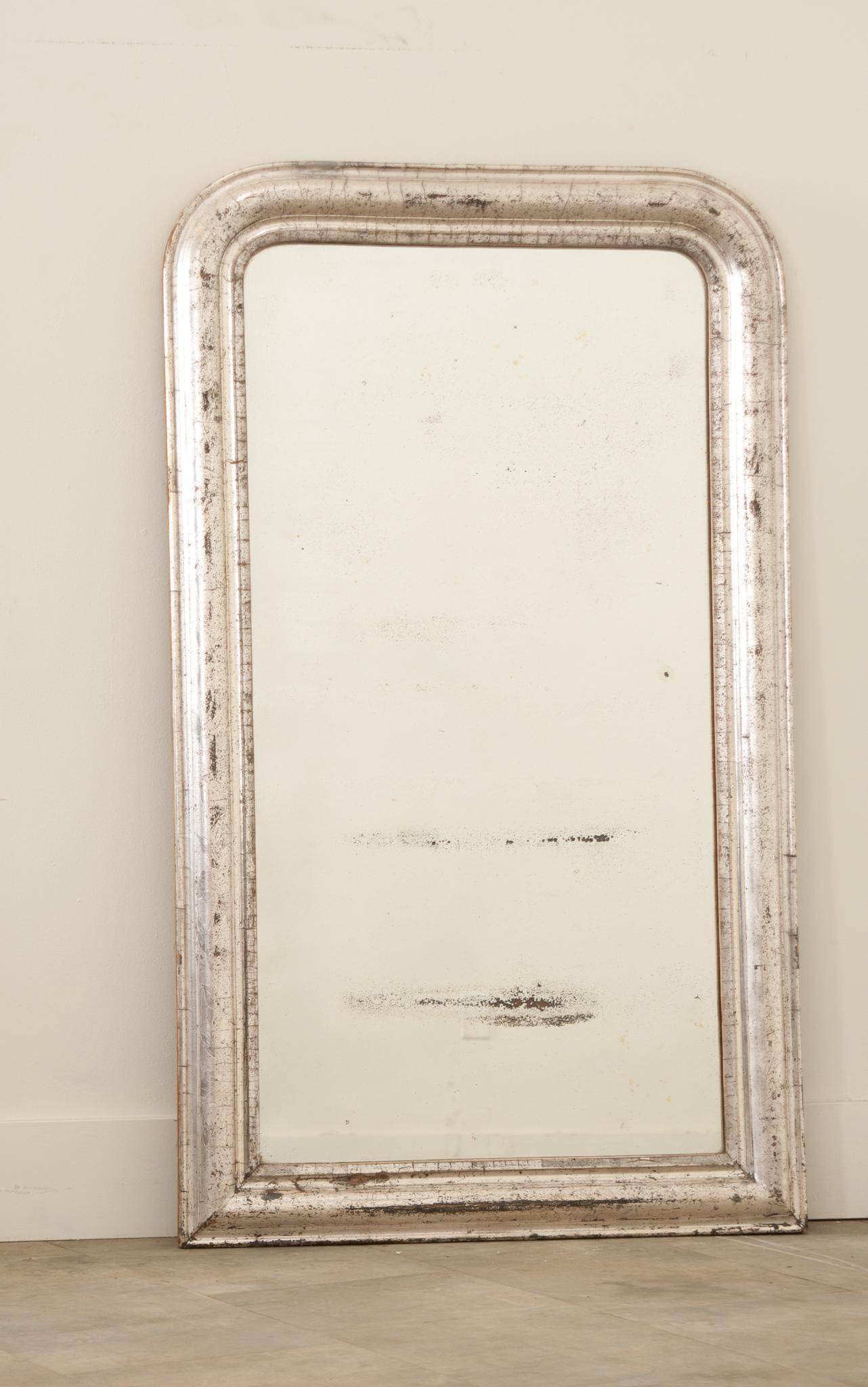 Hand-crafted in France in the 19th Century, this Louis Philippe antique mirror has traditional, timeless lines with rounded corners. The frame is decorated with a luxurious silver leaf finish over a beautiful well patinated gilt frame that is