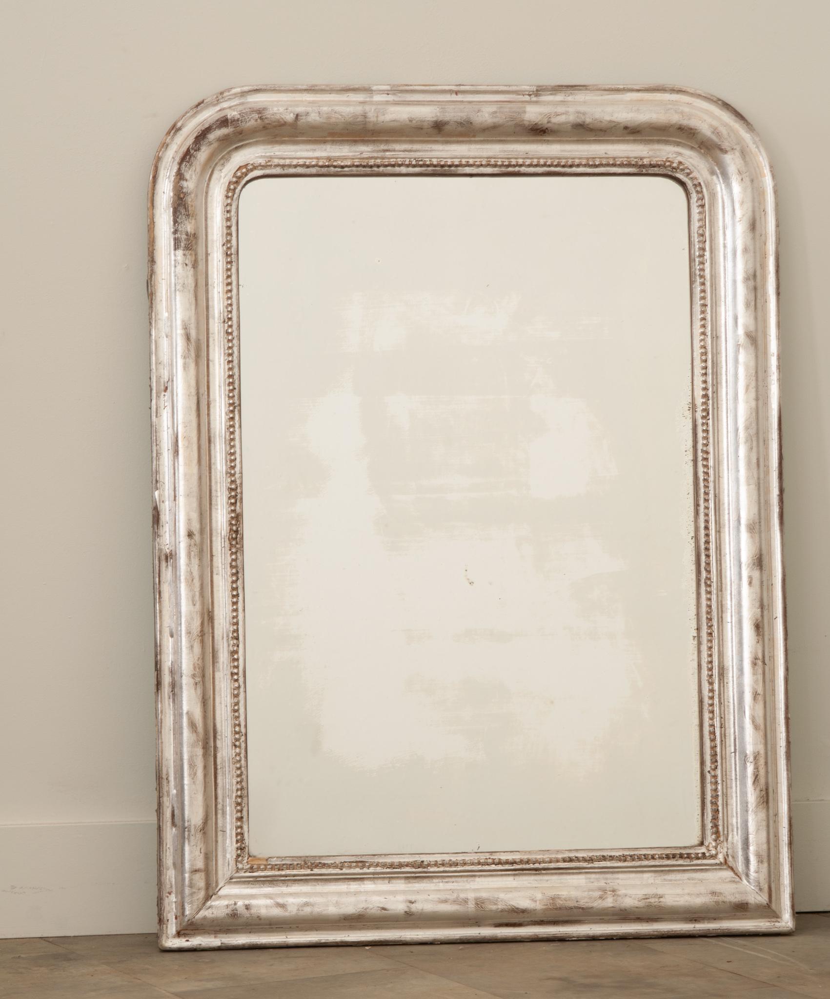 Hand-crafted in France in the 19th Century, this Louis Philippe antique mirror has traditional, timeless lines with rounded corners. The frame is decorated with a luxurious silver leaf finish over beautiful lightly engraved cascading leaf patterns,