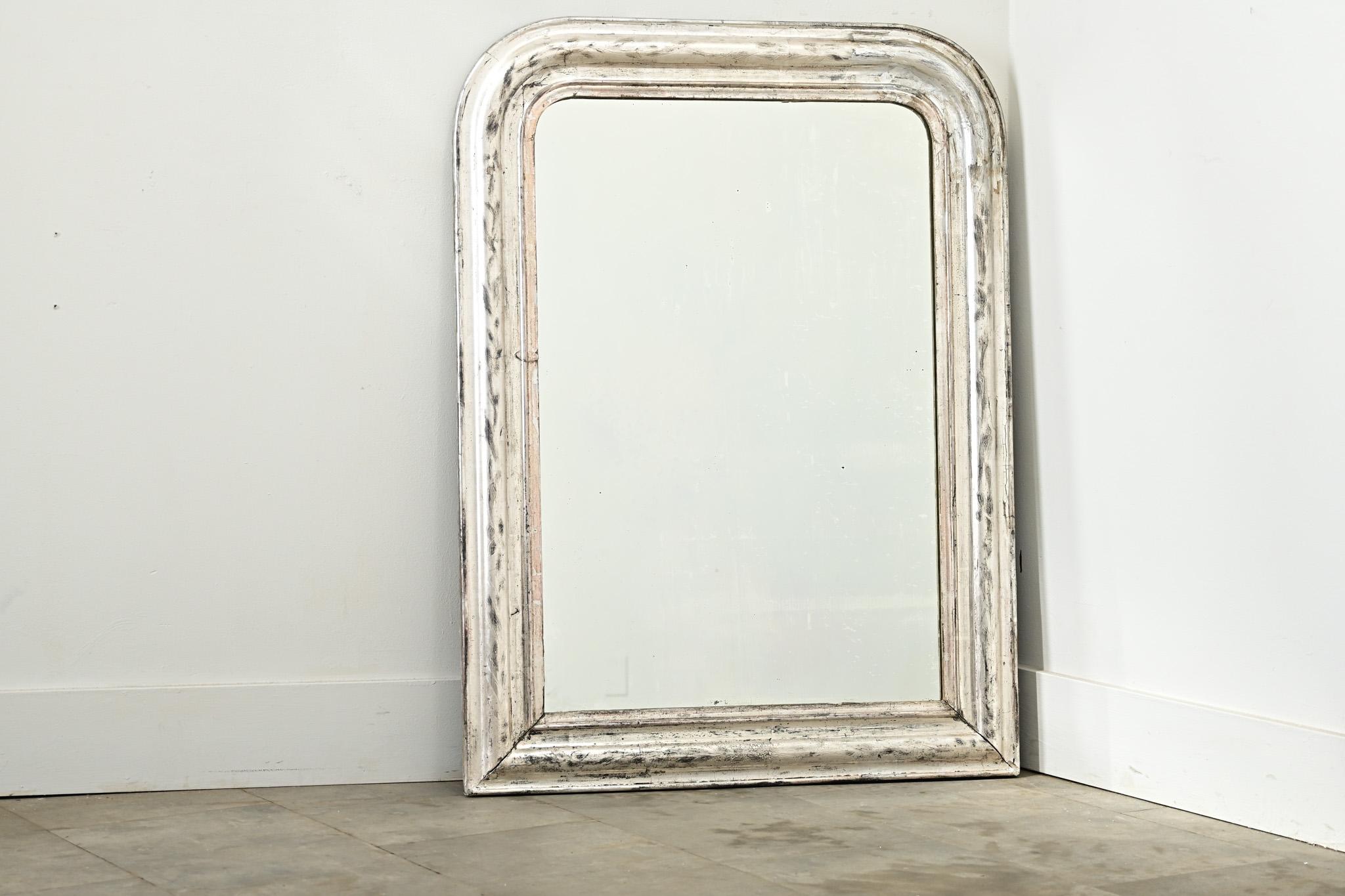 Specchio francese Louis Philippe del XIX secolo con una sobria cornice dorata in argento impreziosita da un'ossidazione scura e da una texture craquelure. Sulla cornice è inciso un elegante motivo floreale a scorrimento, simile a un iris, interrotto