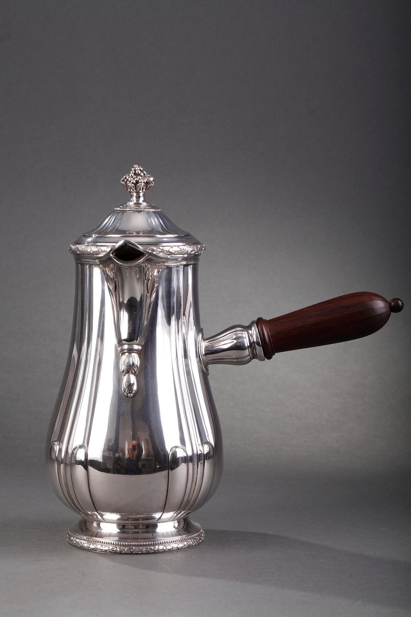 Silver hot chocolate pot decorated with laurel garlands and gadroons. The lid is topped with a fruit bowl, and a rosewood handle is attached to the side.

Silver mark: French Minerve
Silversmith: Puiforcat in Paris.

 Initially a family cutlery