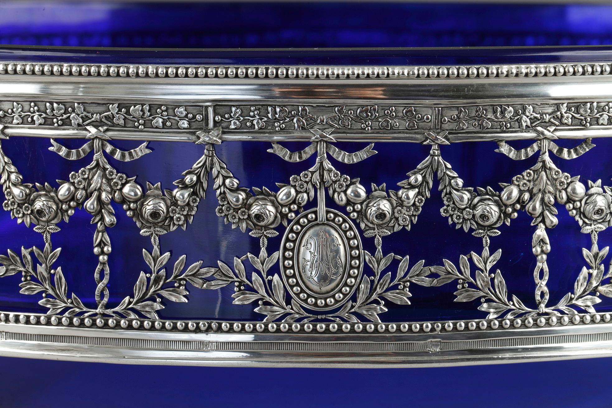 A Silver center of table that can be used as a jardinière. The center of the table rests on four hoofed feet. The collar presents a decoration of floral garlands; Roses, laurel foliage and fruit; Perforated and friezes of vine of vines on a silver