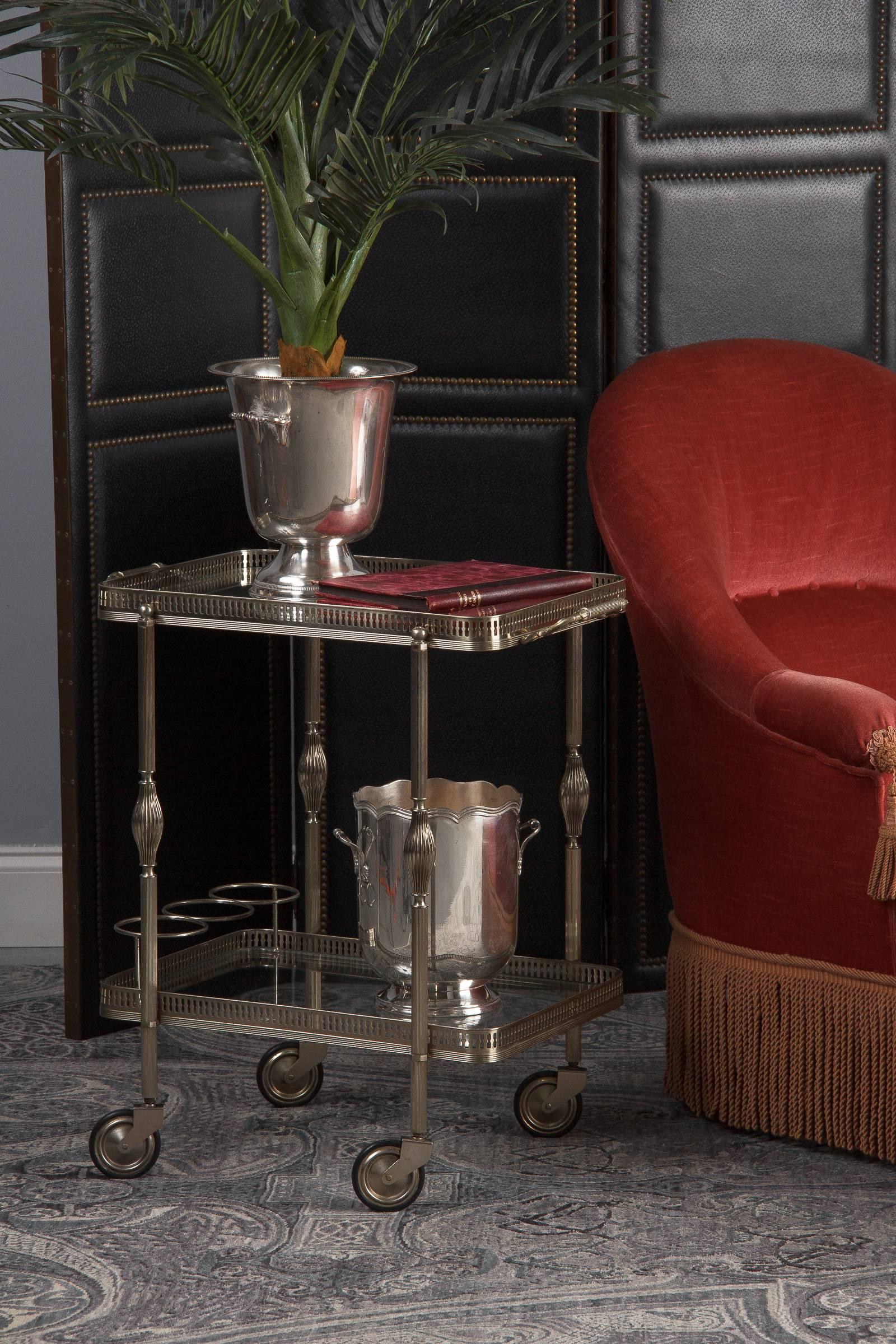 A delightful two-tiered vintage metal and glass French bar cart attributed to Maison Bagues, circa 1950. Silver toned metal frame, possibly nickel, has a slight warm cast to it. Both tiers have pierced metal galleries with ribbed bases. Each leg is