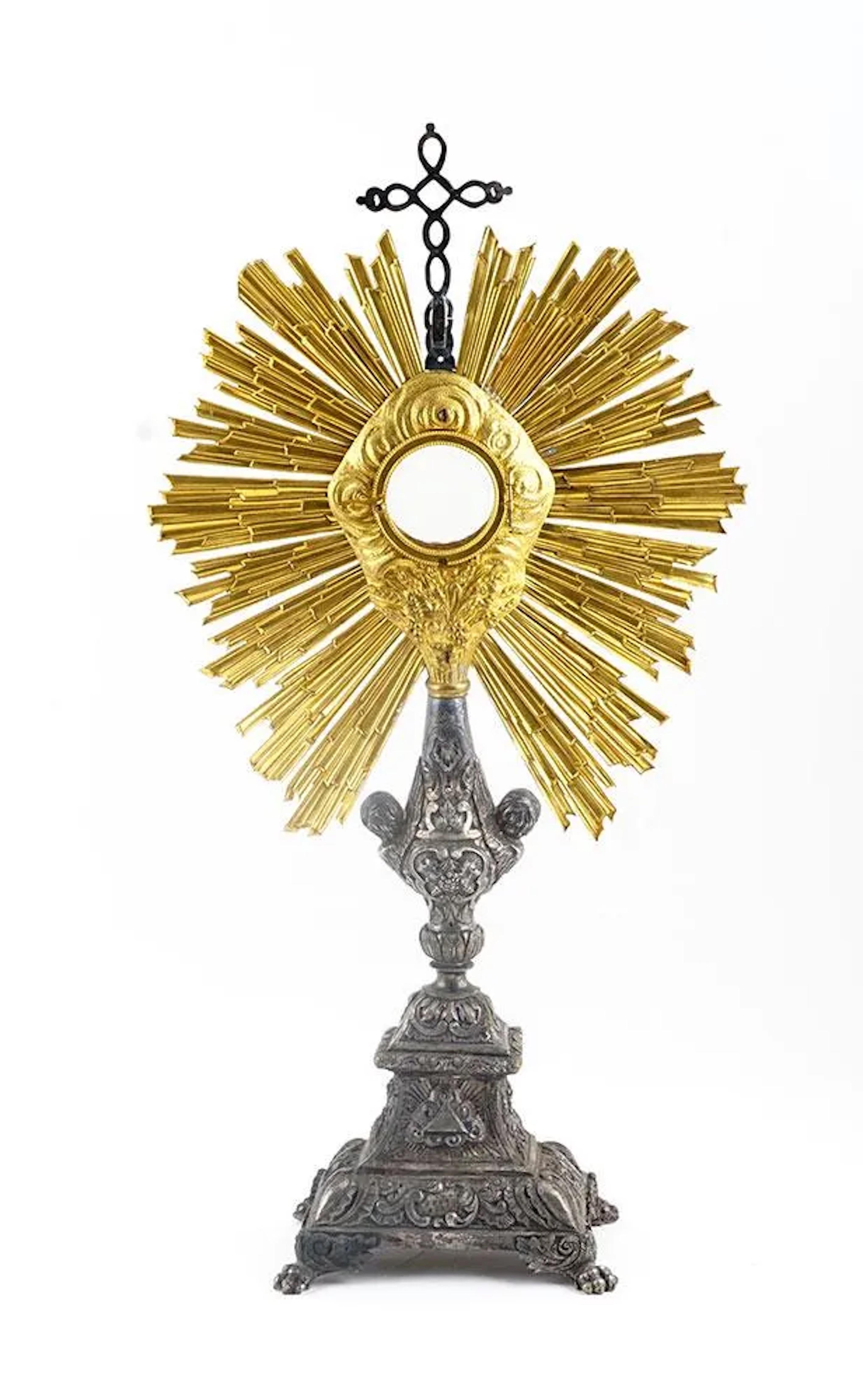 French silver metal and brass monstrance with radiant bezel with baluster shaft with cherub heads resting on rectangular base decorated claw feet.
 