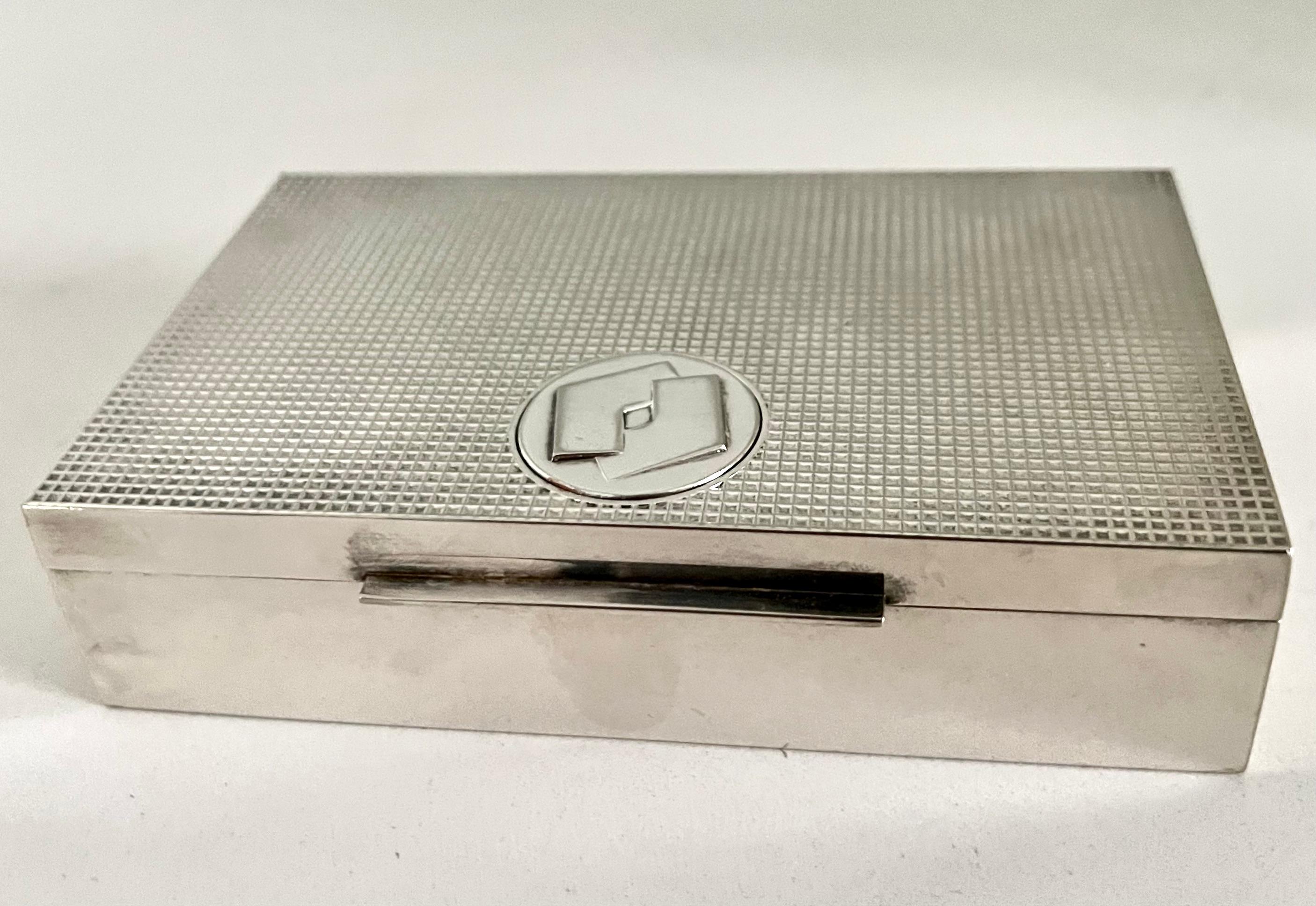 Lovely silver plate box with a suede interior. the box has an unknown emblem on the top front center and the Waffle pattern on top makes this box unique and a compliment to any cocktail table. Can also be used on a desk to hold small items. Perhaps