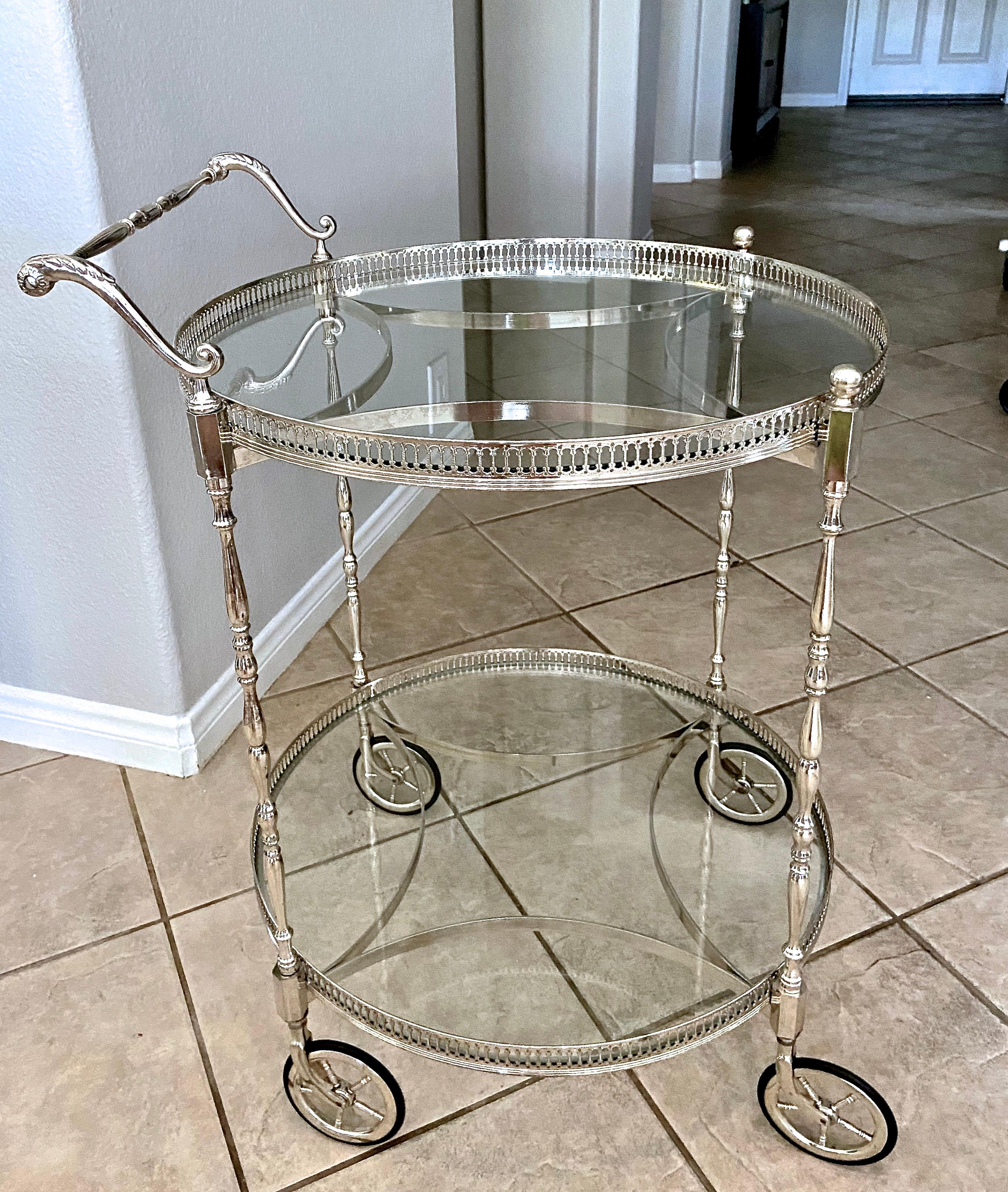 French neoclassic style 2 tier nickel plated round bar cart with inset glass shelves. The polished nickel plating is in great overall condition. High quality workmanship throughout including refined delicate gallery railing, turned leg supports and