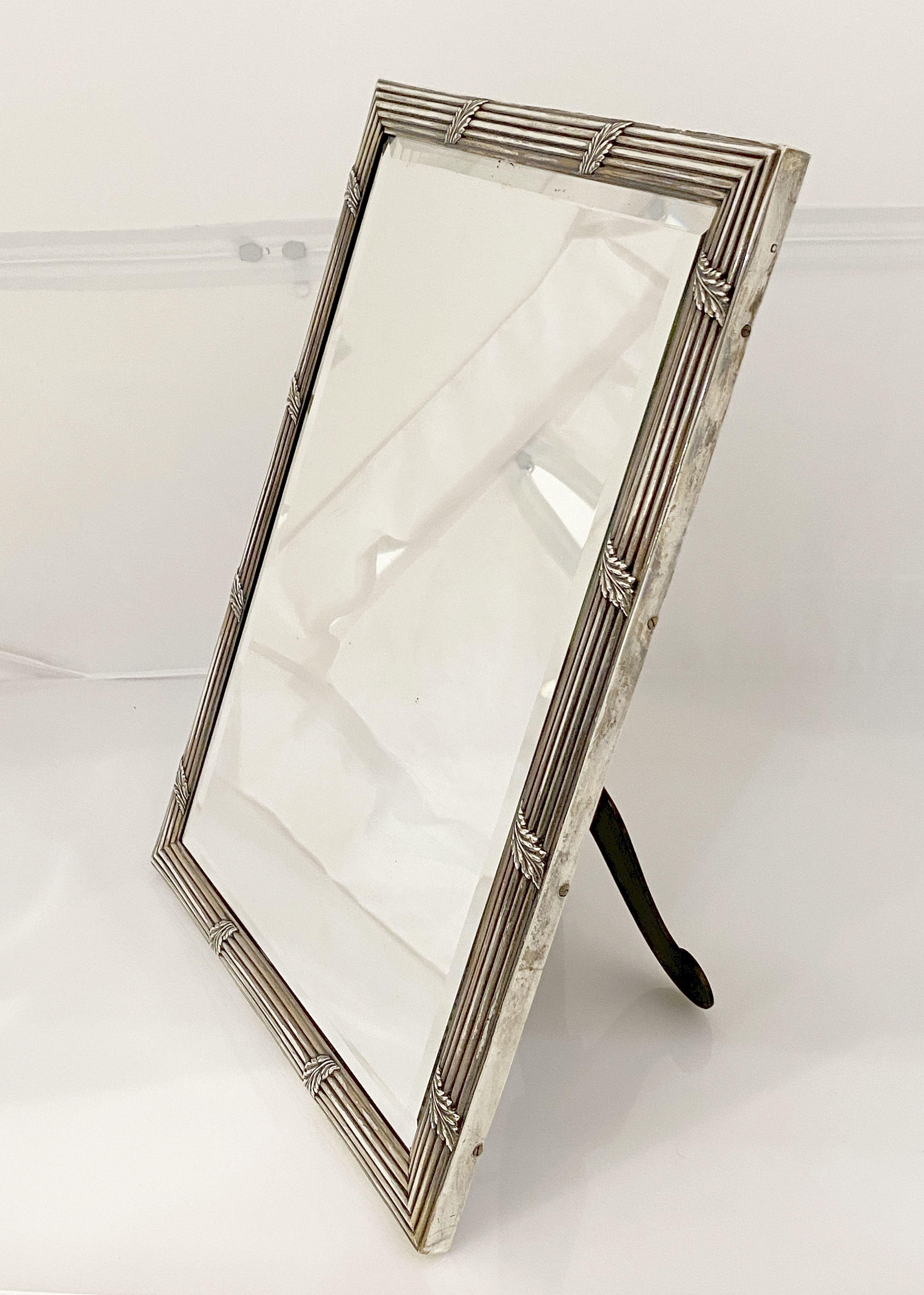 An elegant French vanity or tabletop mirror of fine silver, featuring a Neo-Classical relief design to the frame, enclosing a rectangular beveled mirror, back of wood with folding brass support stand.

Can be mounted on a wall or used as a vanity