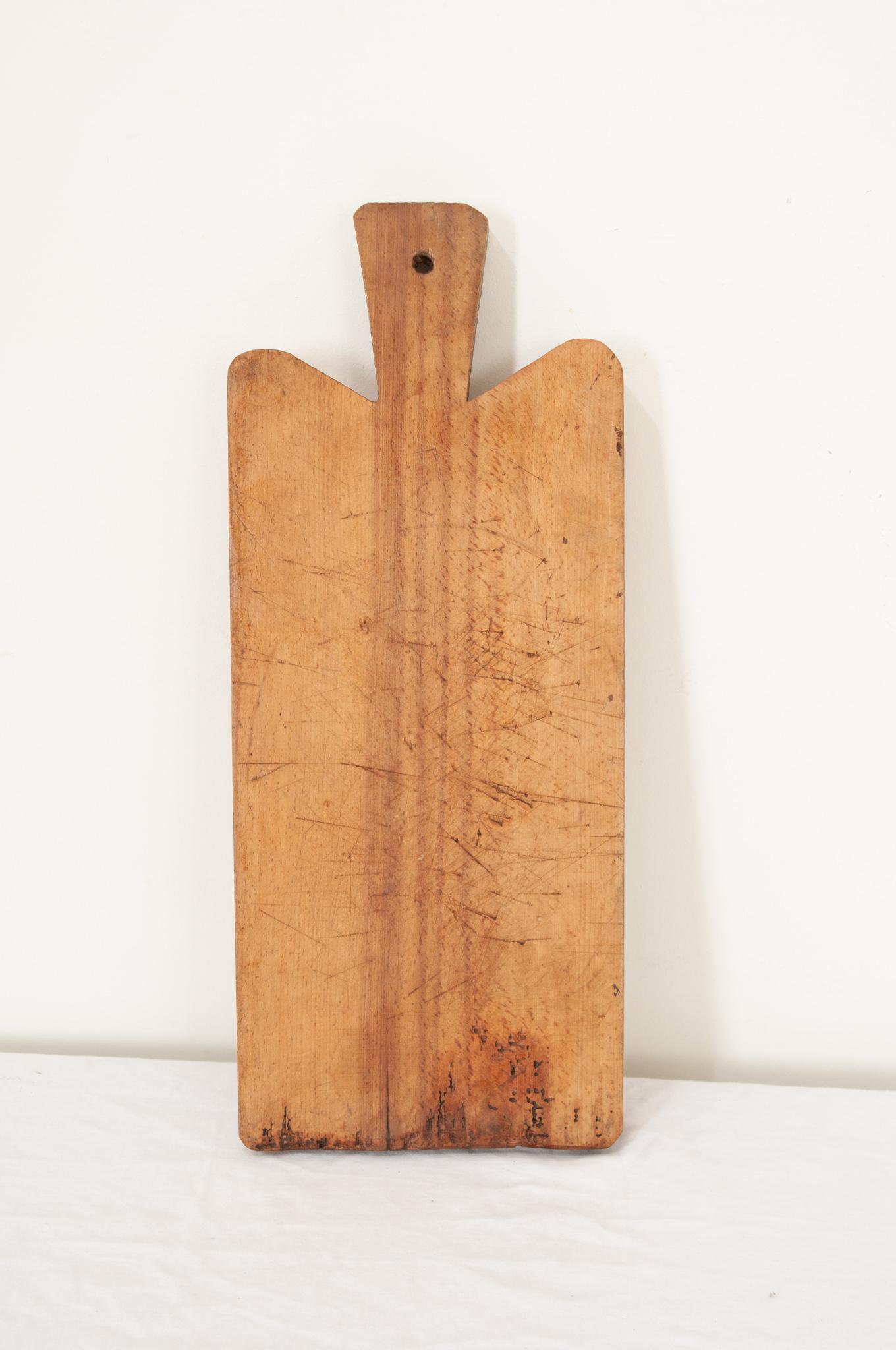 Ein Schneidebrett aus Massivholz aus Frankreich in rechteckiger Form mit glatten Ecken und einem Griff. Das abgenutzte Brett ist aus einem einzigen Stück Holz gefertigt, das nun eine hervorragende Patina aufweist. Messerabdrücke und Kratzer, die von