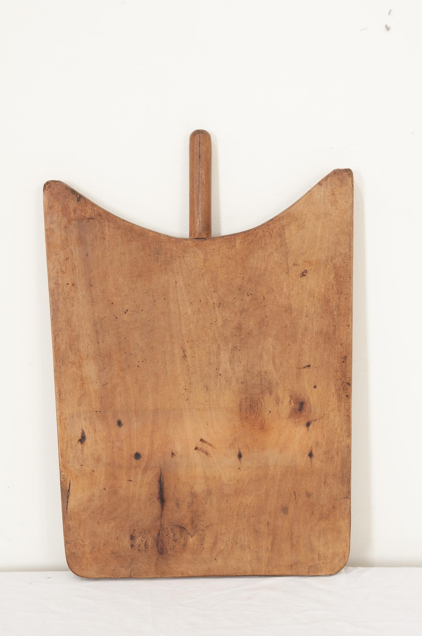 A large single plank wood cutting board from France in an interesting shape with smooth corners and a handle. Knife marks and scrapes that were left by cooks, now long gone, can be seen and felt as if they were made yesterday. A nice antique, full