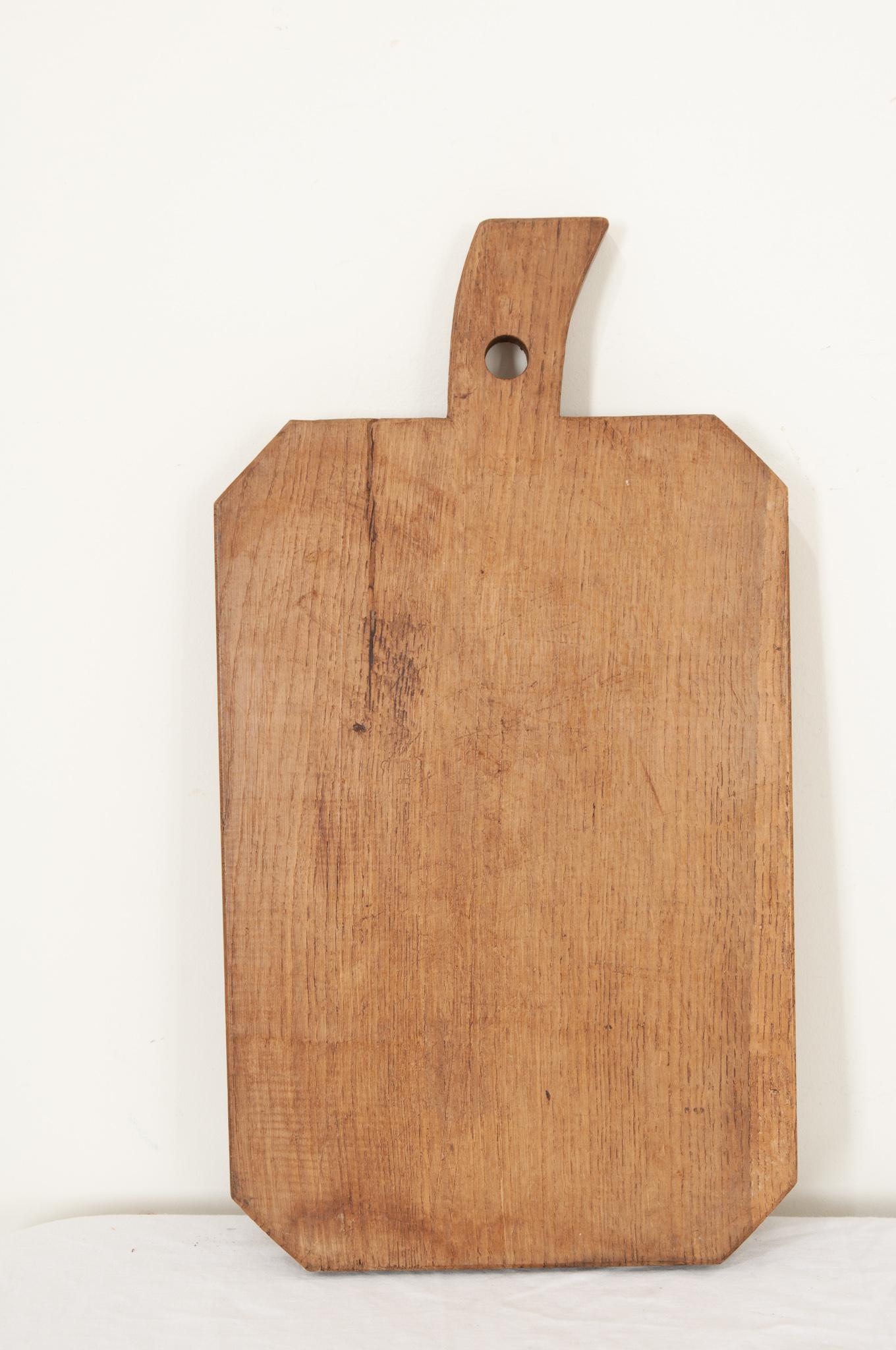 Ein großes Holzschneidebrett aus Frankreich in einer interessanten Form mit abgeschrägten Ecken und einem Griff in Form eines Stiels. Messerabdrücke und Kratzer, die von längst verstorbenen Köchen hinterlassen wurden, sind zu sehen und zu spüren,