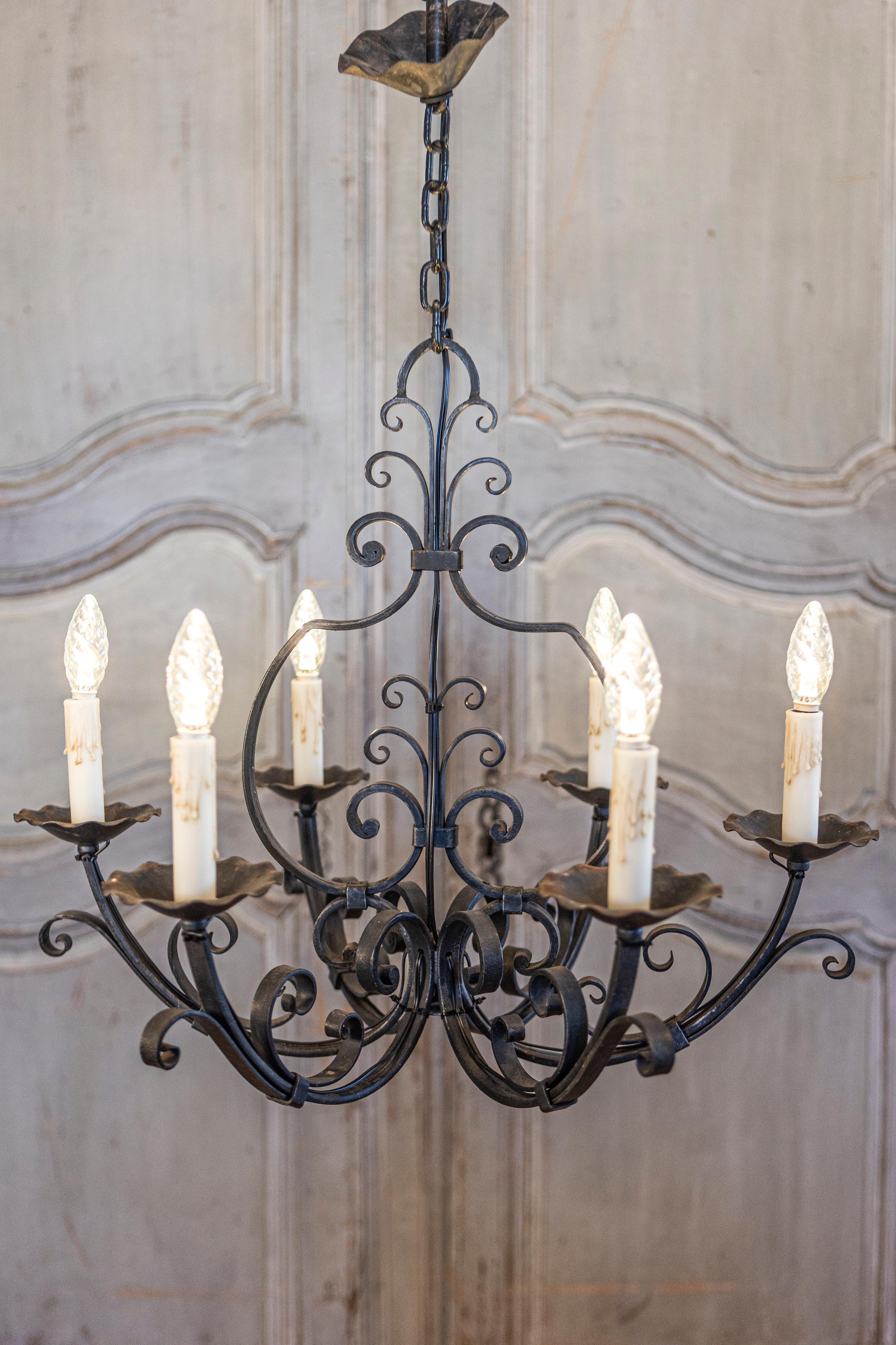 A French wrought iron chandelier from the 20th century with six lights and scrolling motifs, professionally rewired for the USA. This exquisite French wrought iron chandelier from the 20th century embodies elegance and intricate craftsmanship.