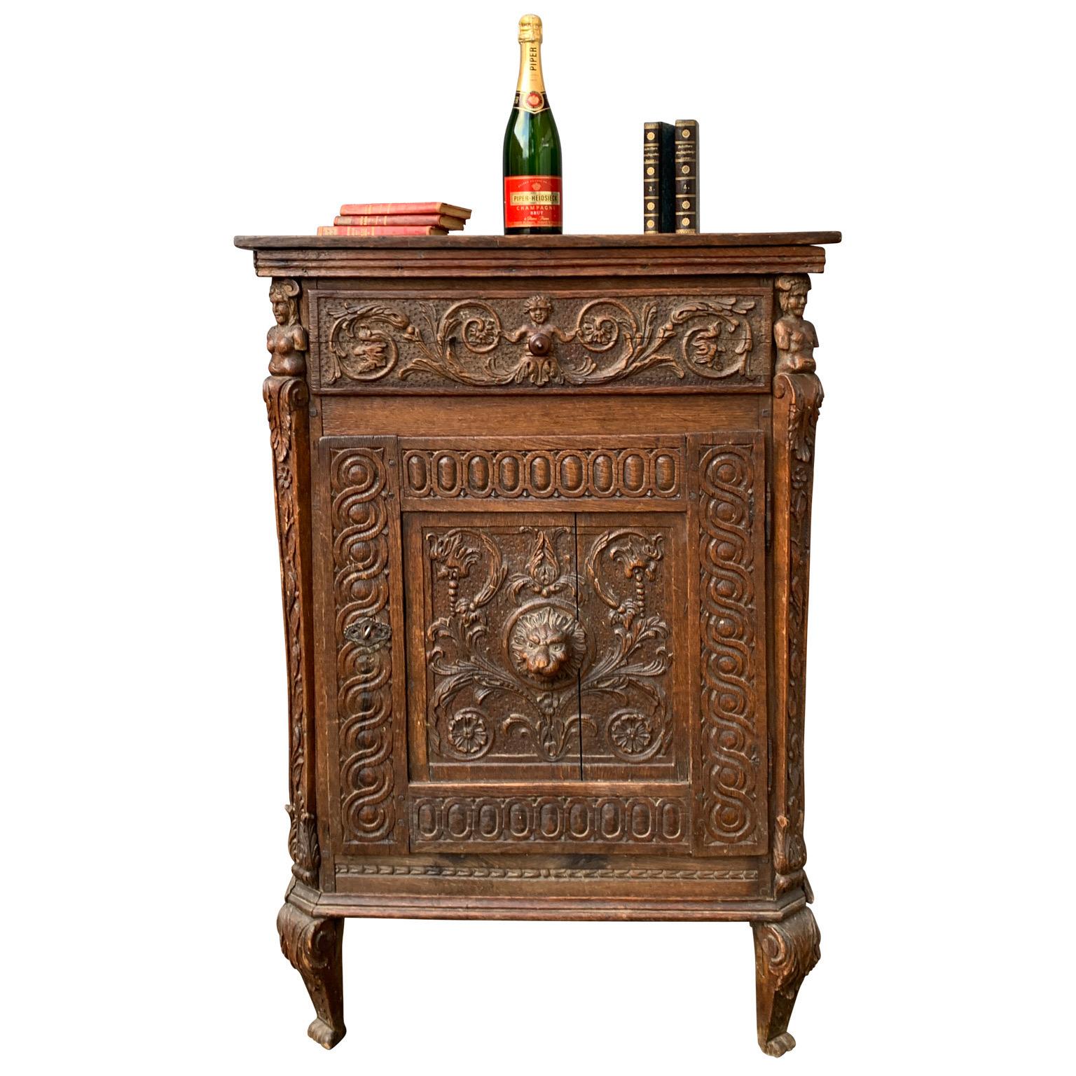 European small carved baroque cabinet in oak wood, France circa 1680-1730. This hand carved cabinet has one drawer and a door. This piece features a lion head as a knob on the door, a putti on the drawer and caryatids figures on the corners. The
