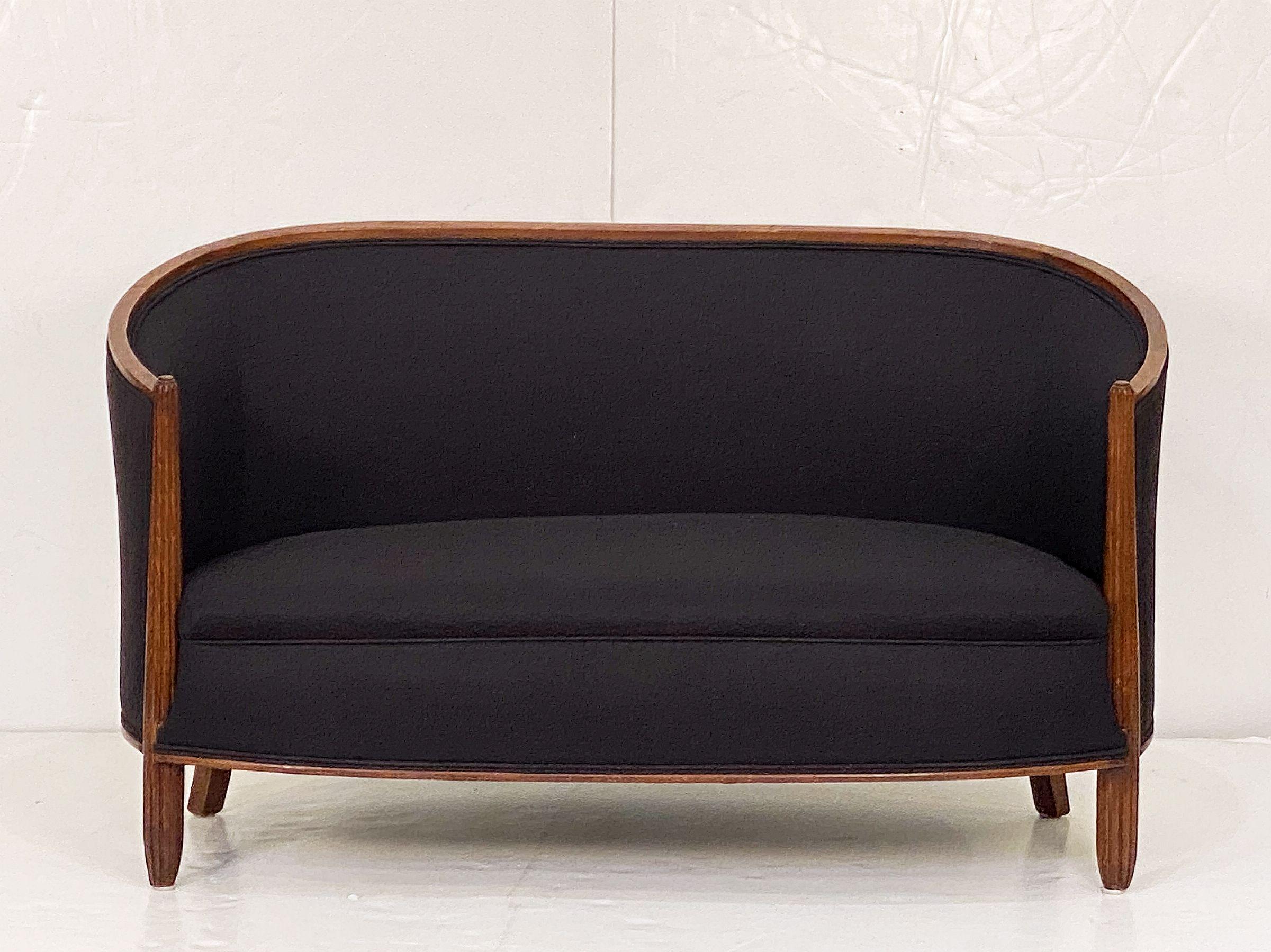 A beautiful French sofa or settee upholstered in black linen, featuring a rounded back and curved arms, with a comfortable seat, resting on four legs, with a gracefully turned rail around the back and decoratively reeded facing legs.

A matching