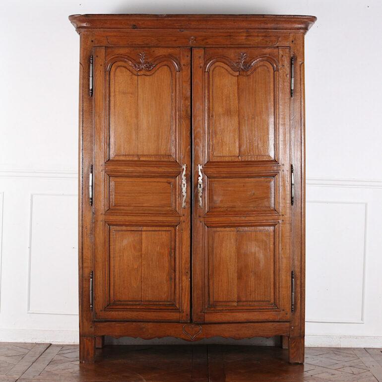 An early-19th century French two-door armoire in oak. A simple rustic country piece with paneled sides and doors with some simple carved details. Shelving to the interior. C. 1820 – 40.